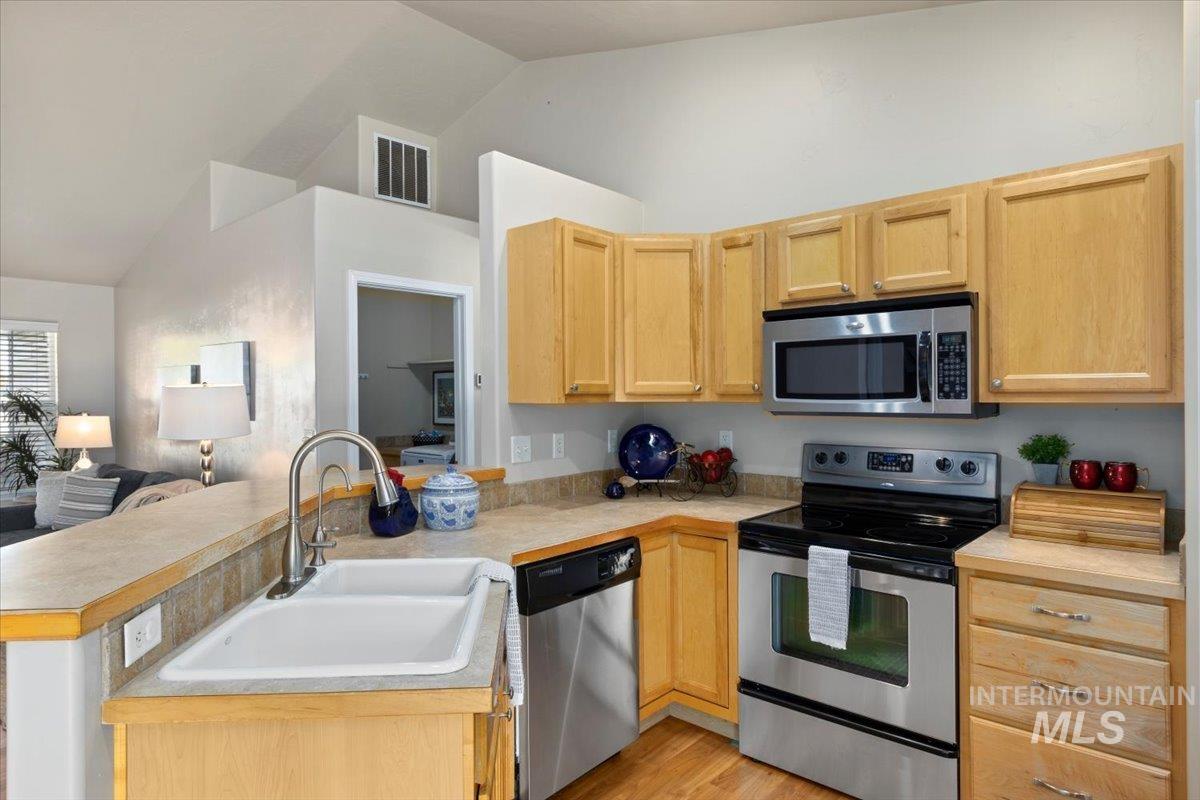 Kitchen with stainless steel appliances, light countertops, light brown cabinetry, lofted ceiling, and a peninsula