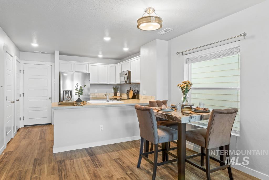 Kitchen with white cabinets, light wood-type flooring, appliances with stainless steel finishes, light countertops, and a peninsula