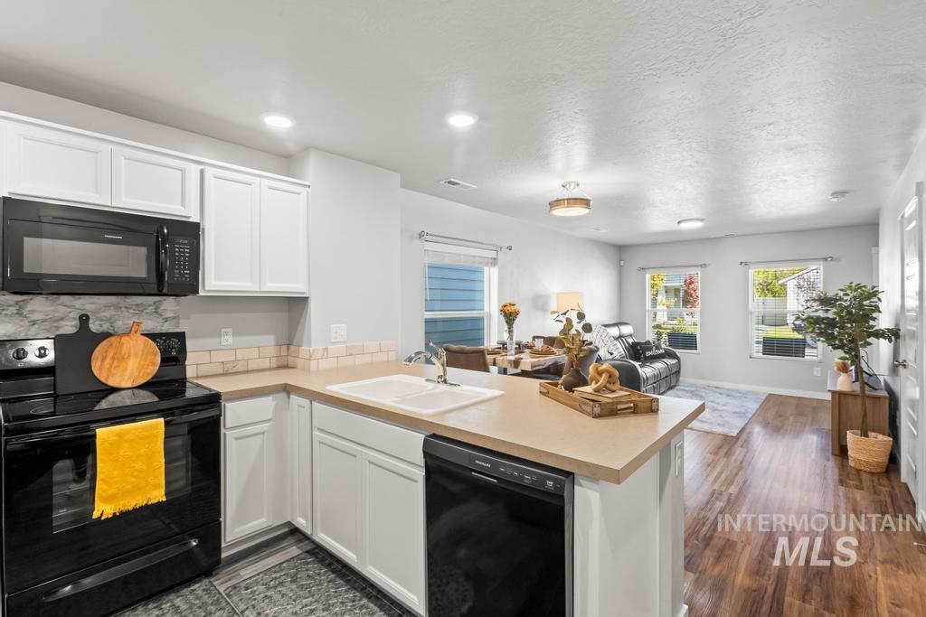 Kitchen featuring black appliances, light countertops, open floor plan, white cabinets, and a textured ceiling