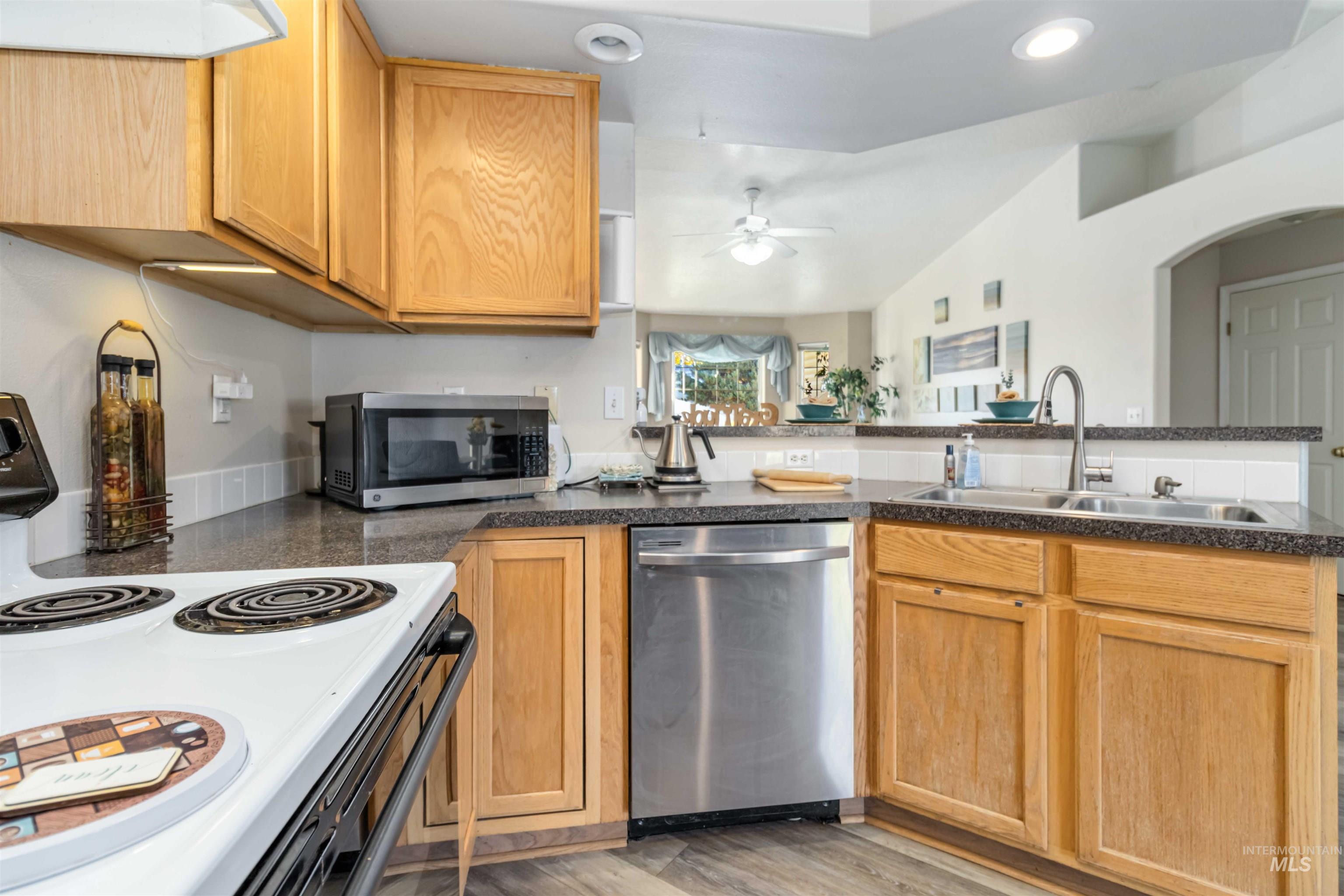 Kitchen featuring appliances with stainless steel finishes, light wood-type flooring, dark countertops, recessed lighting, and ceiling fan