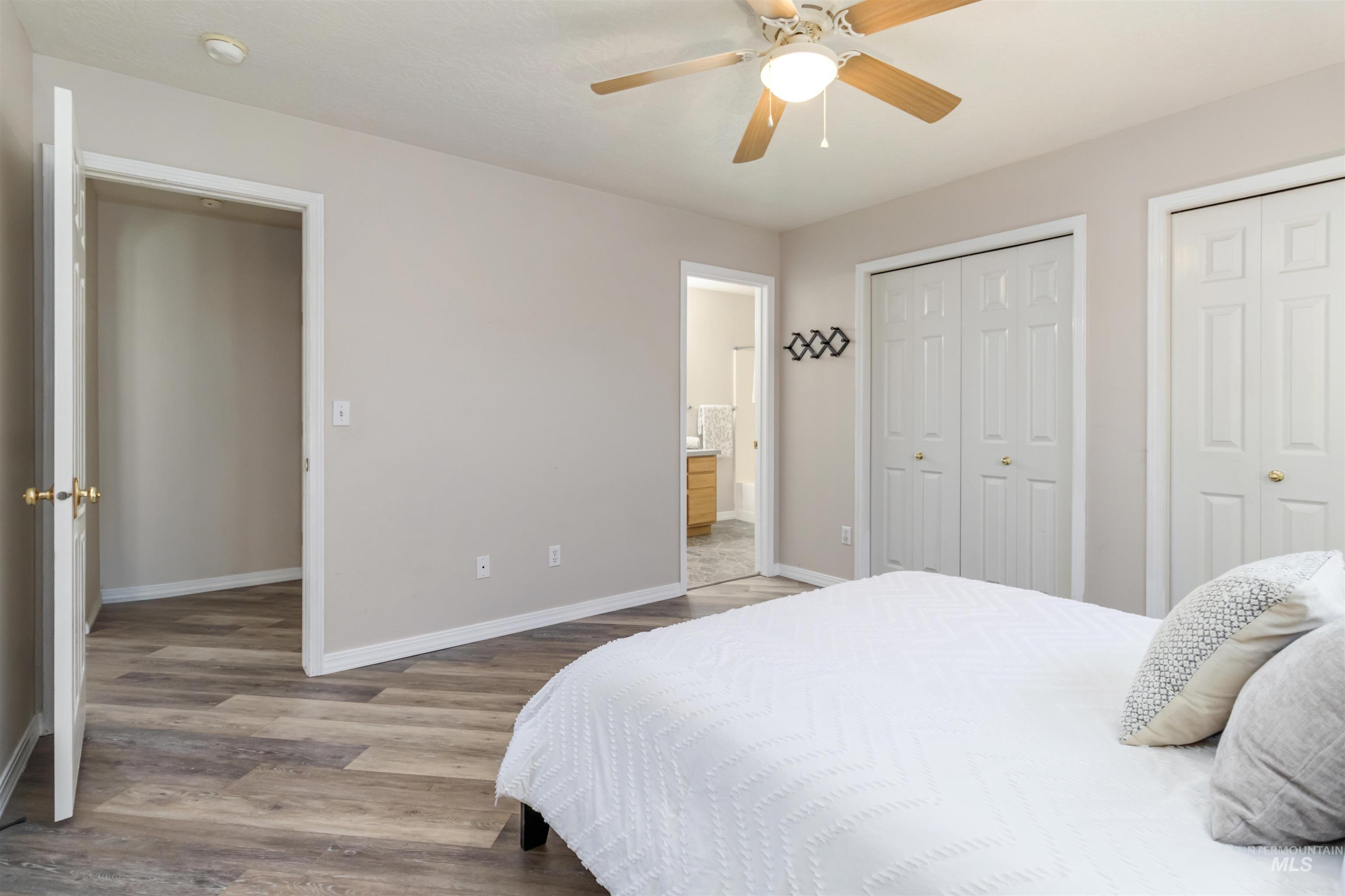 Bedroom with two closets, light wood-style floors, a ceiling fan, and ensuite bathroom