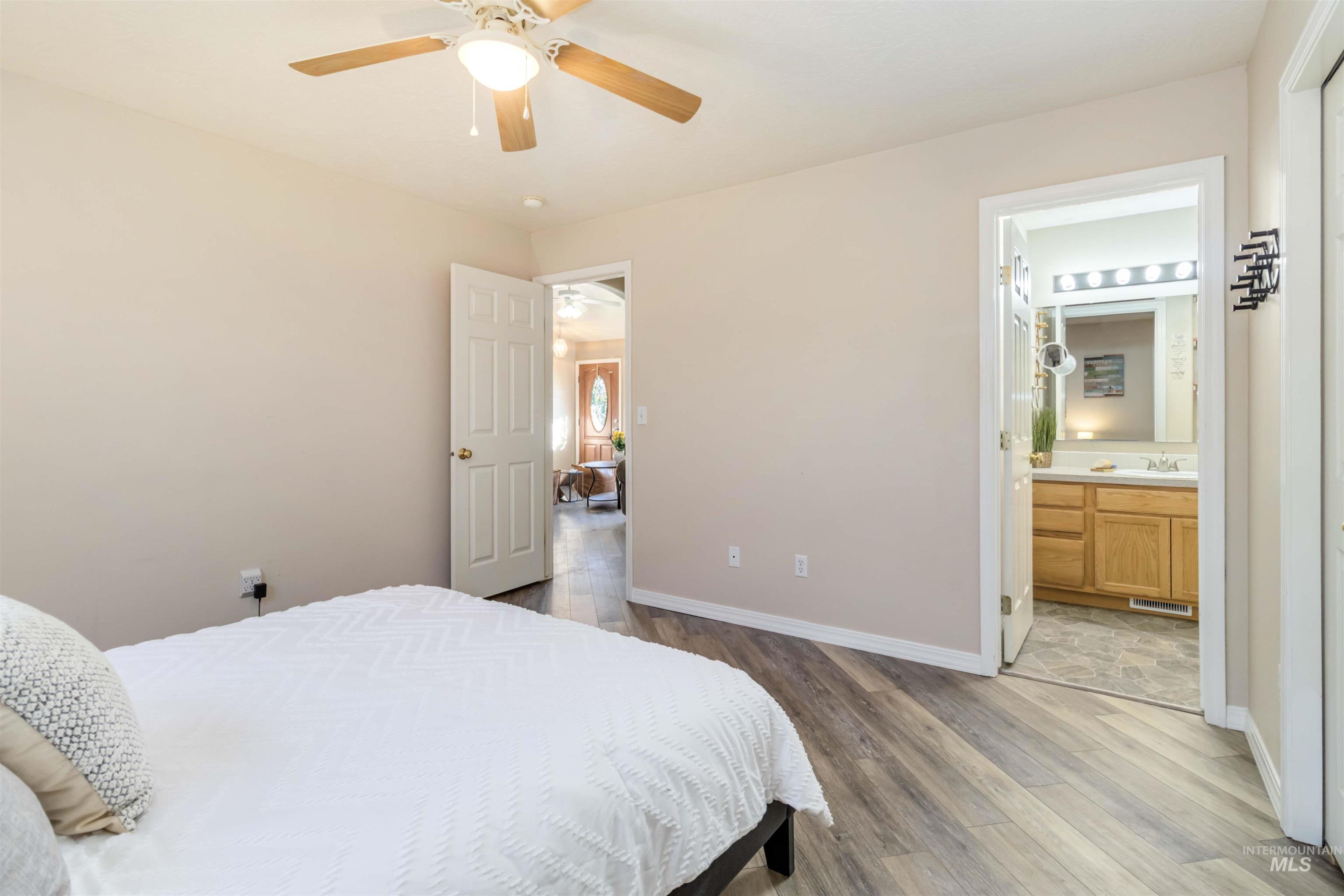 Bedroom featuring light wood-style flooring, ceiling fan, and ensuite bath