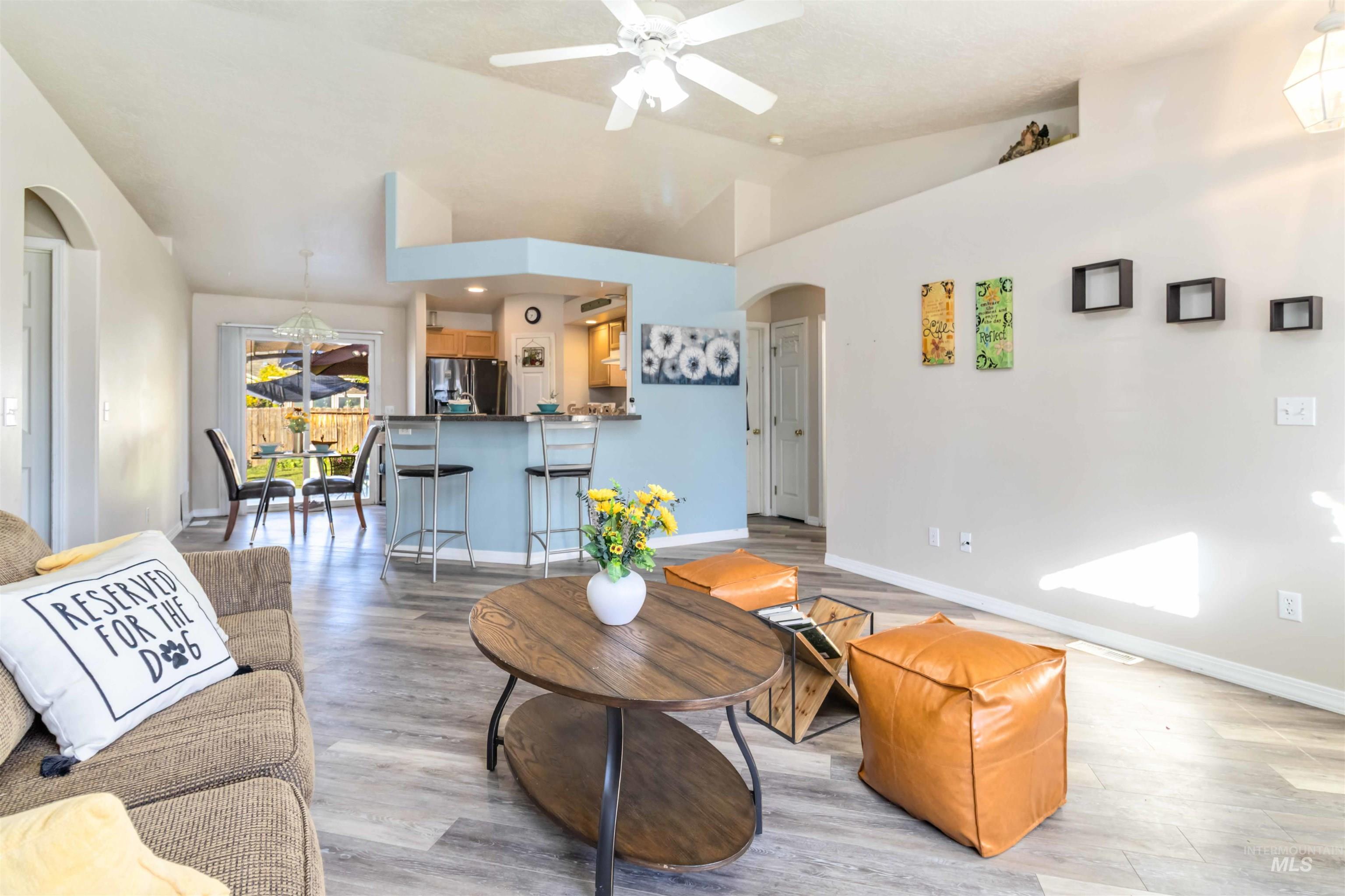 Living room with arched walkways, light wood-type flooring, vaulted ceiling, and a ceiling fan