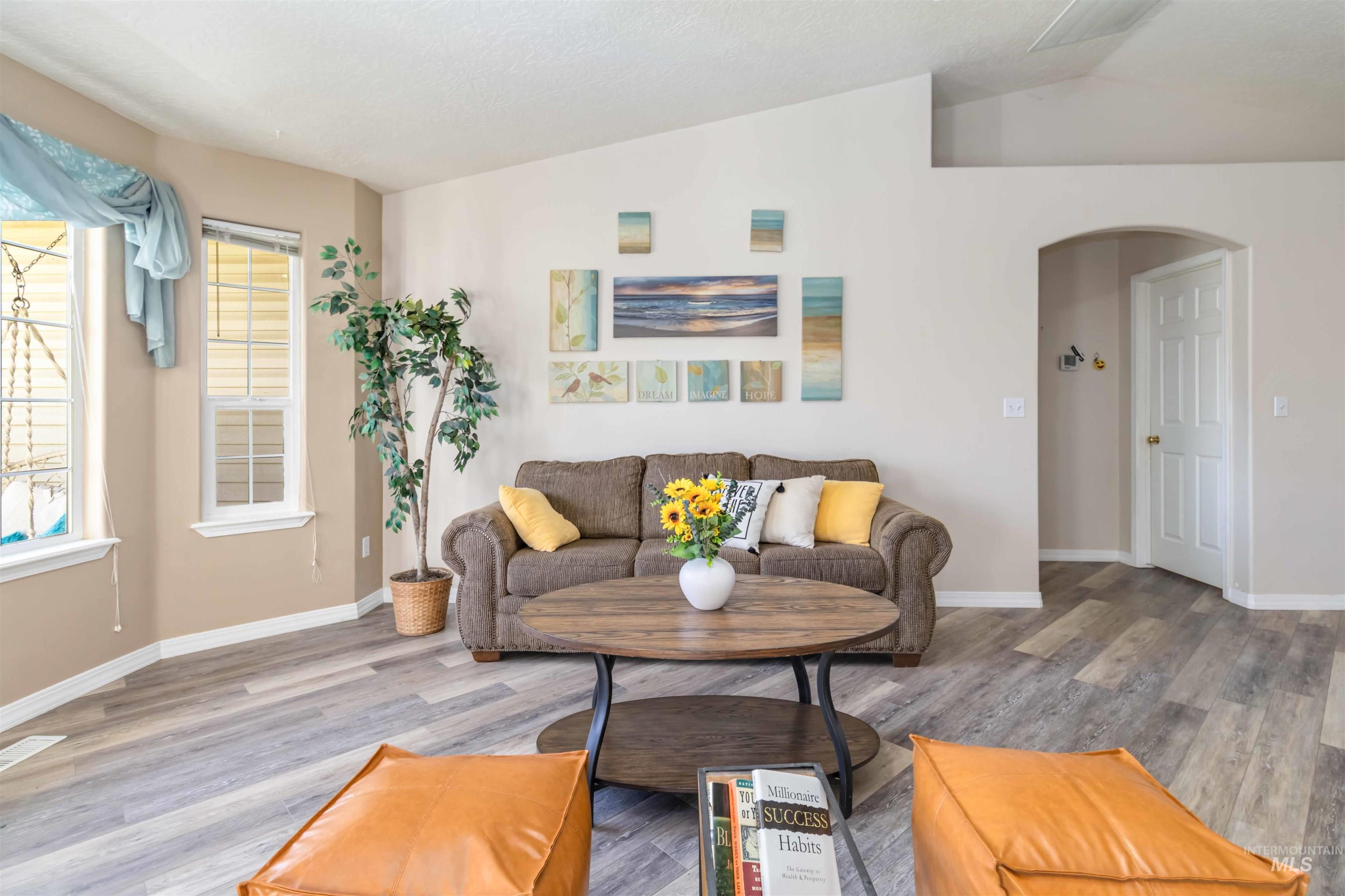 Living area with lofted ceiling, arched walkways, and wood finished floors