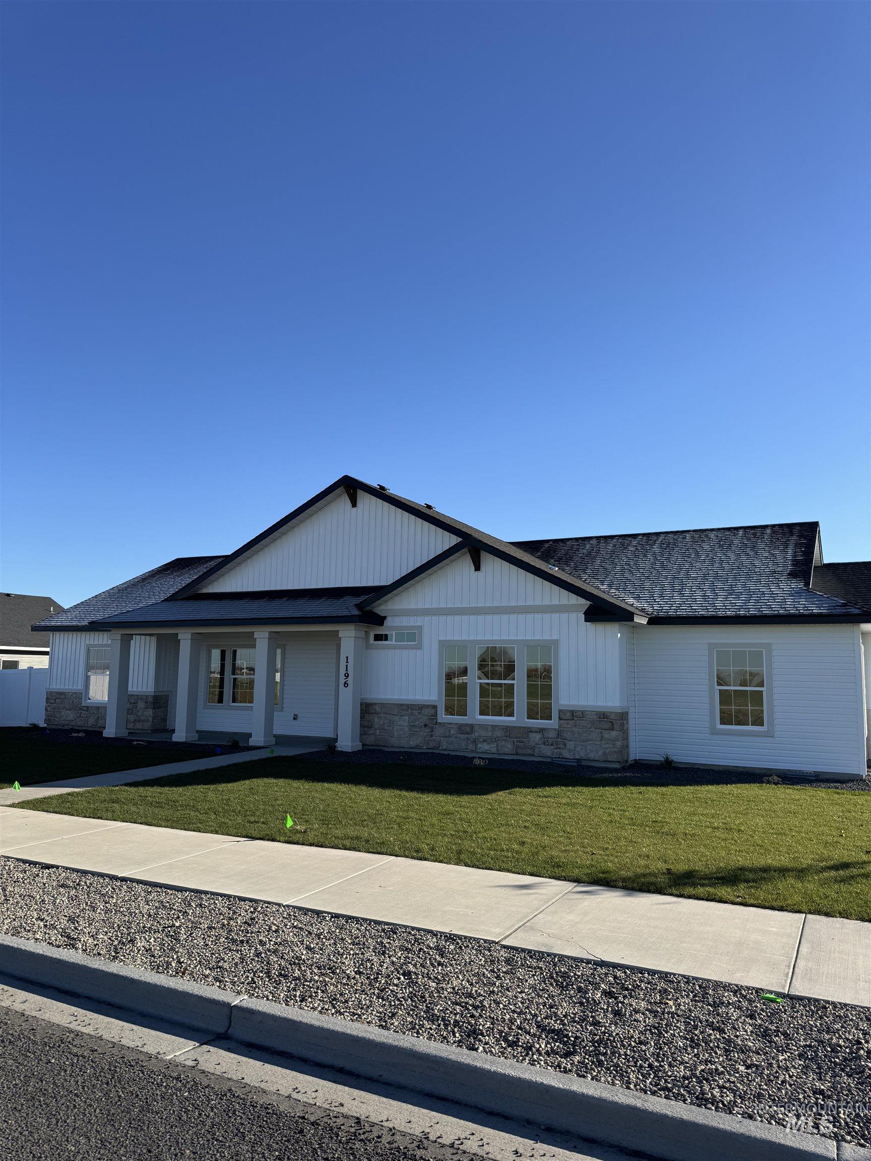View of front of home with stone siding, a front yard, a shingled roof, and a porch