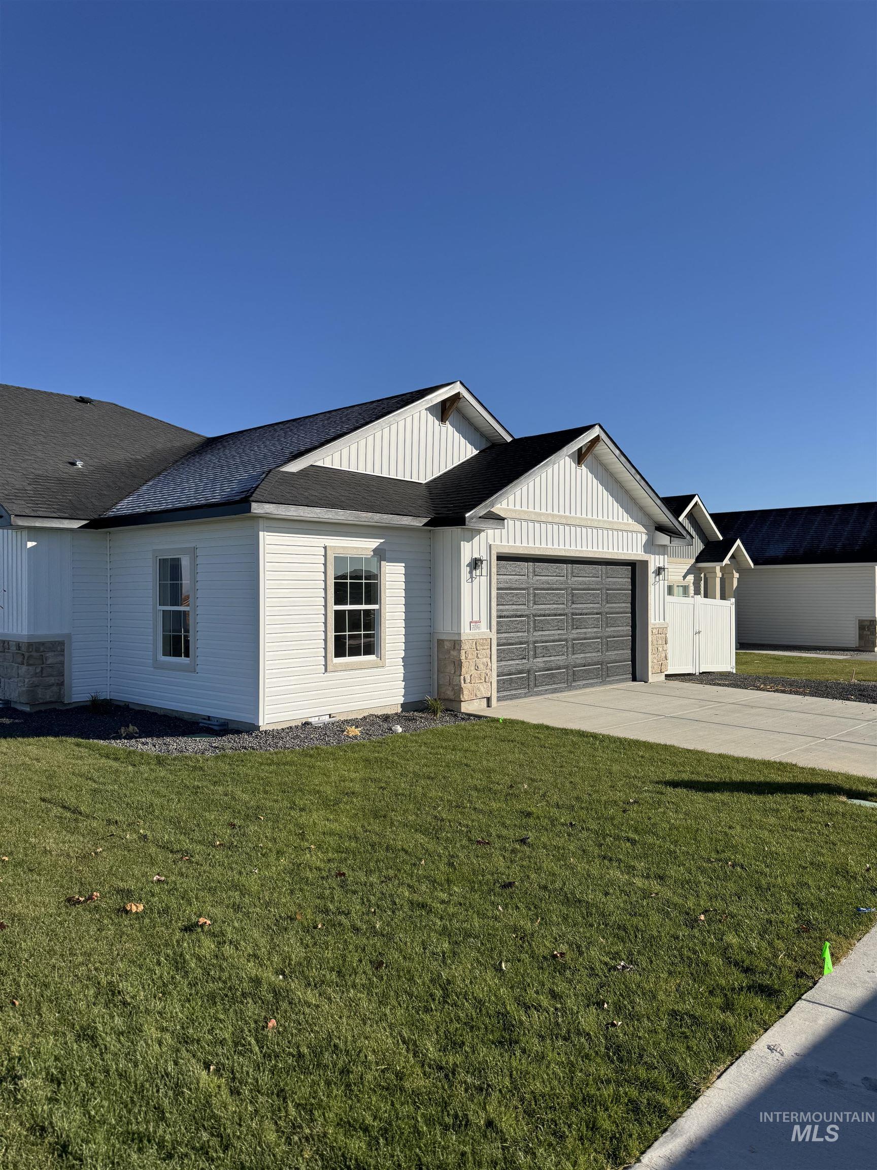 View of front of property featuring concrete driveway, board and batten siding, a garage, a front yard, and stone siding