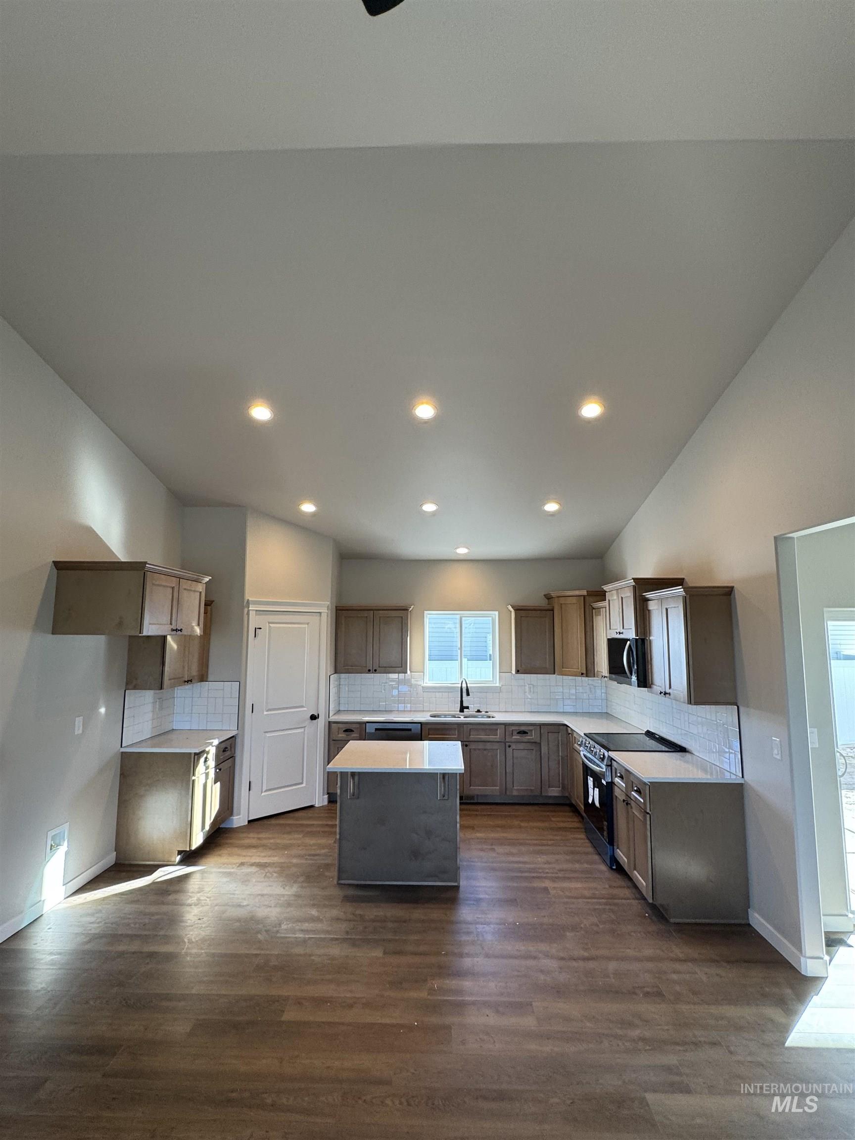 Kitchen with decorative backsplash, a center island, stainless steel appliances, lofted ceiling, and dark wood-type flooring
