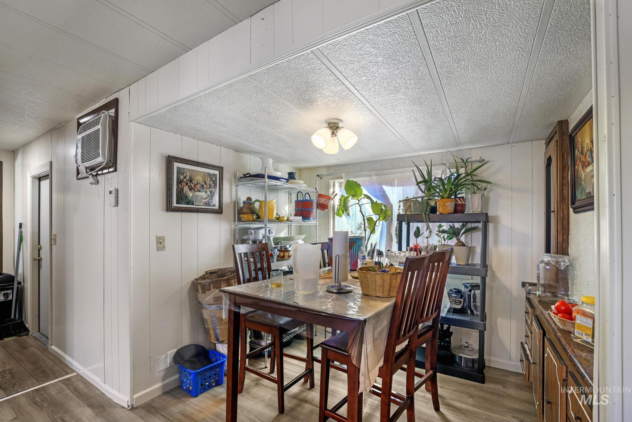 Dining space featuring light wood-style floors, wooden walls, an AC wall unit, and a textured ceiling