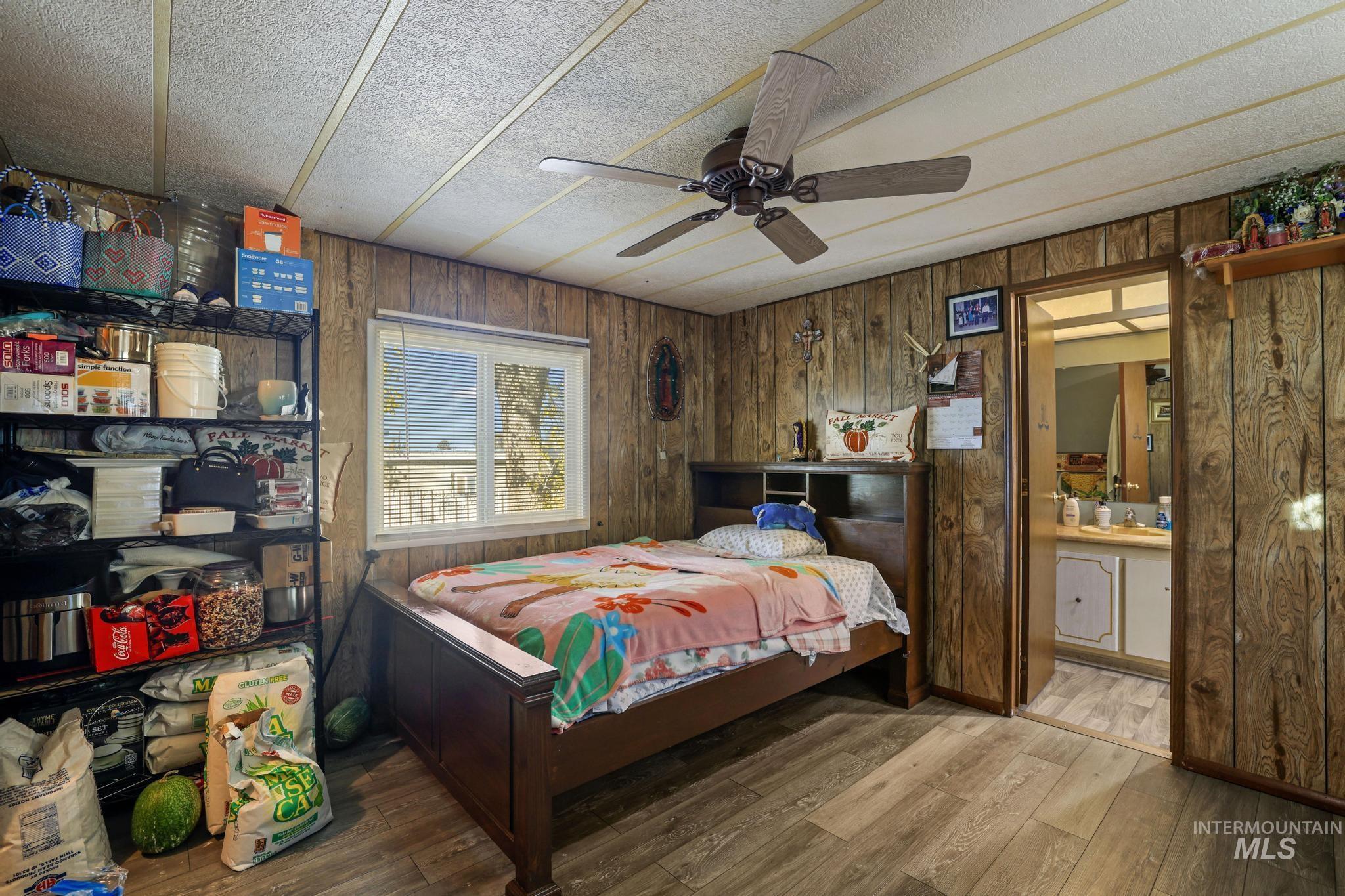 Bedroom with wooden walls, hardwood / wood-style floors, ceiling fan, ensuite bathroom, and a textured ceiling