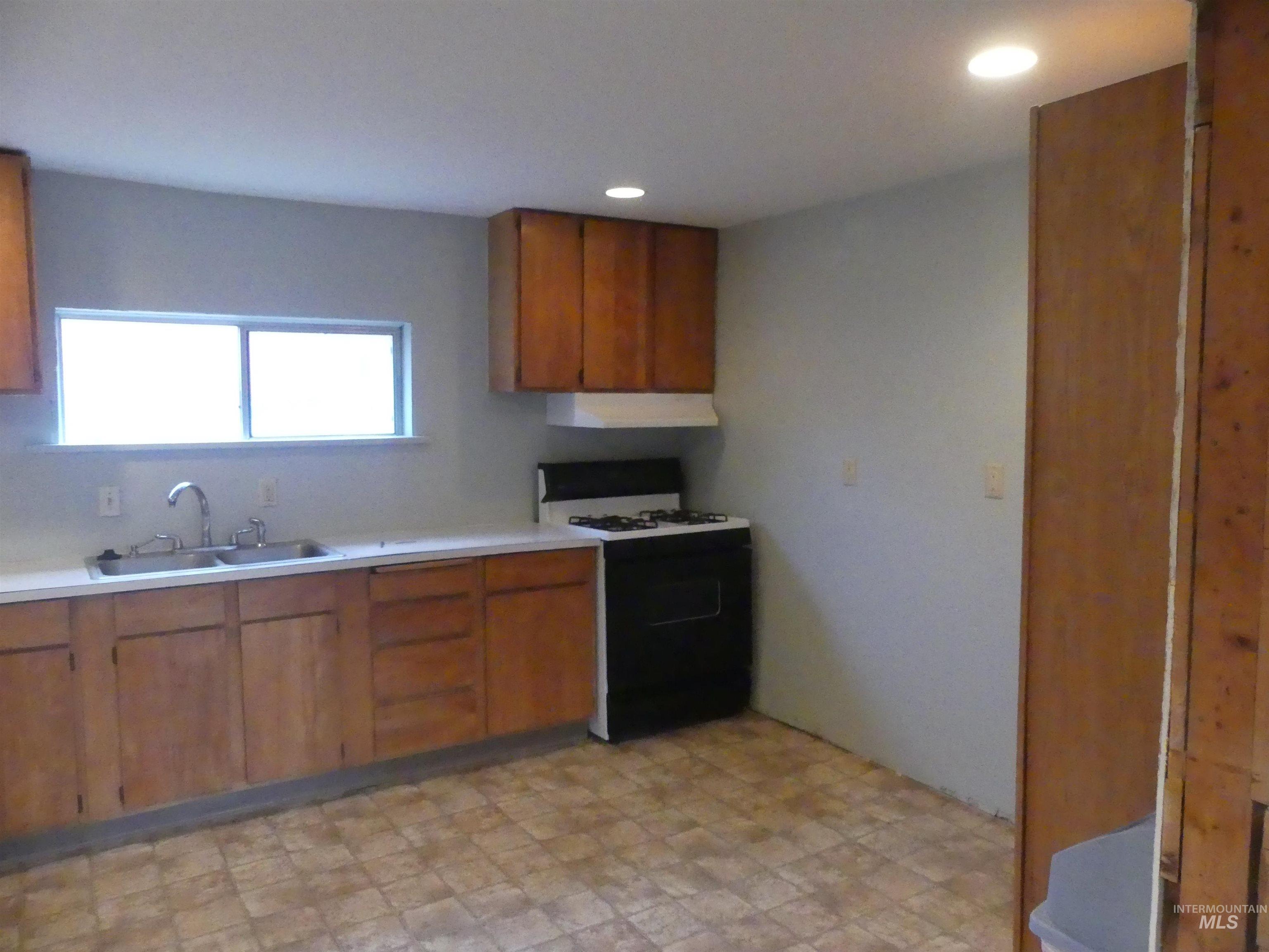 Kitchen featuring brown cabinets, light countertops, gas stove, ventilation hood, and recessed lighting