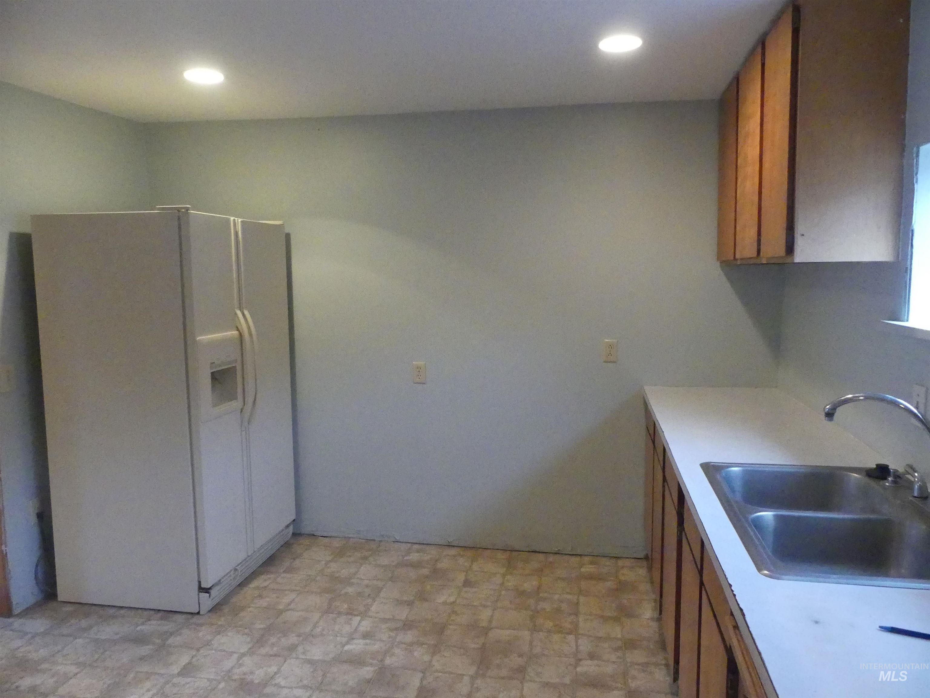 Kitchen featuring brown cabinets, white refrigerator with ice dispenser, light countertops, and recessed lighting