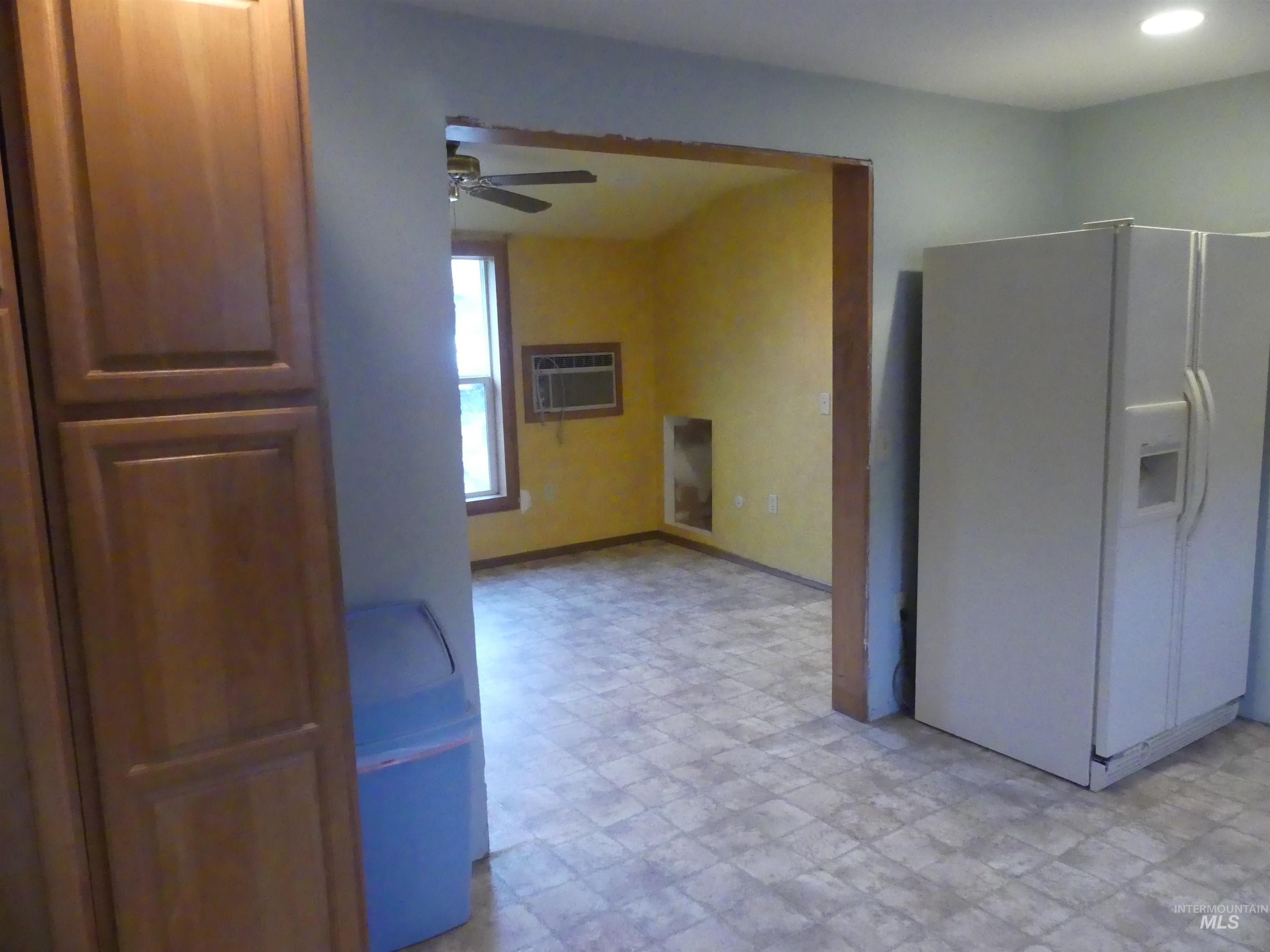 Kitchen with white fridge with ice dispenser, ceiling fan, a wall unit AC, and light floors