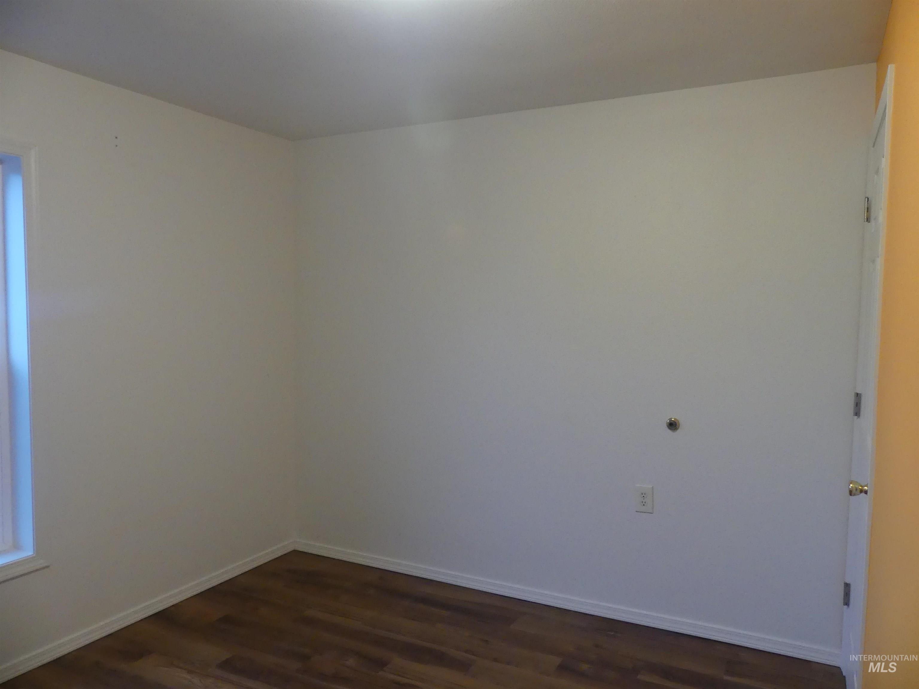 Unfurnished room with baseboards and dark wood-type flooring