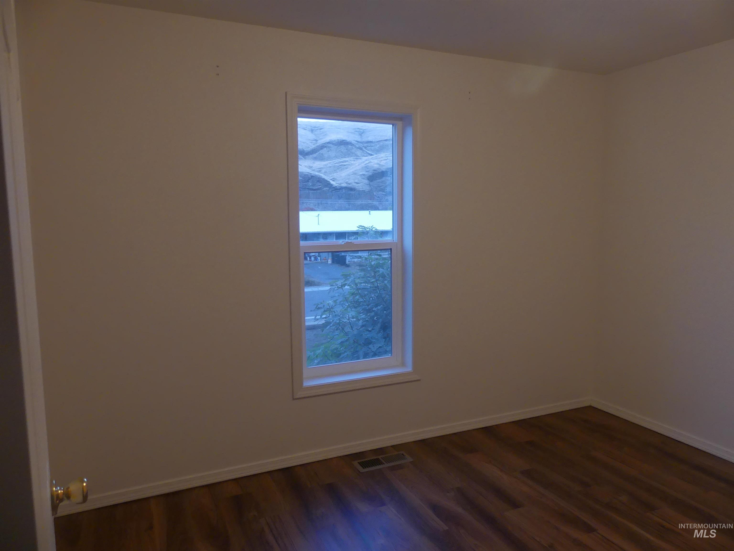 Spare room featuring baseboards and dark wood-type flooring