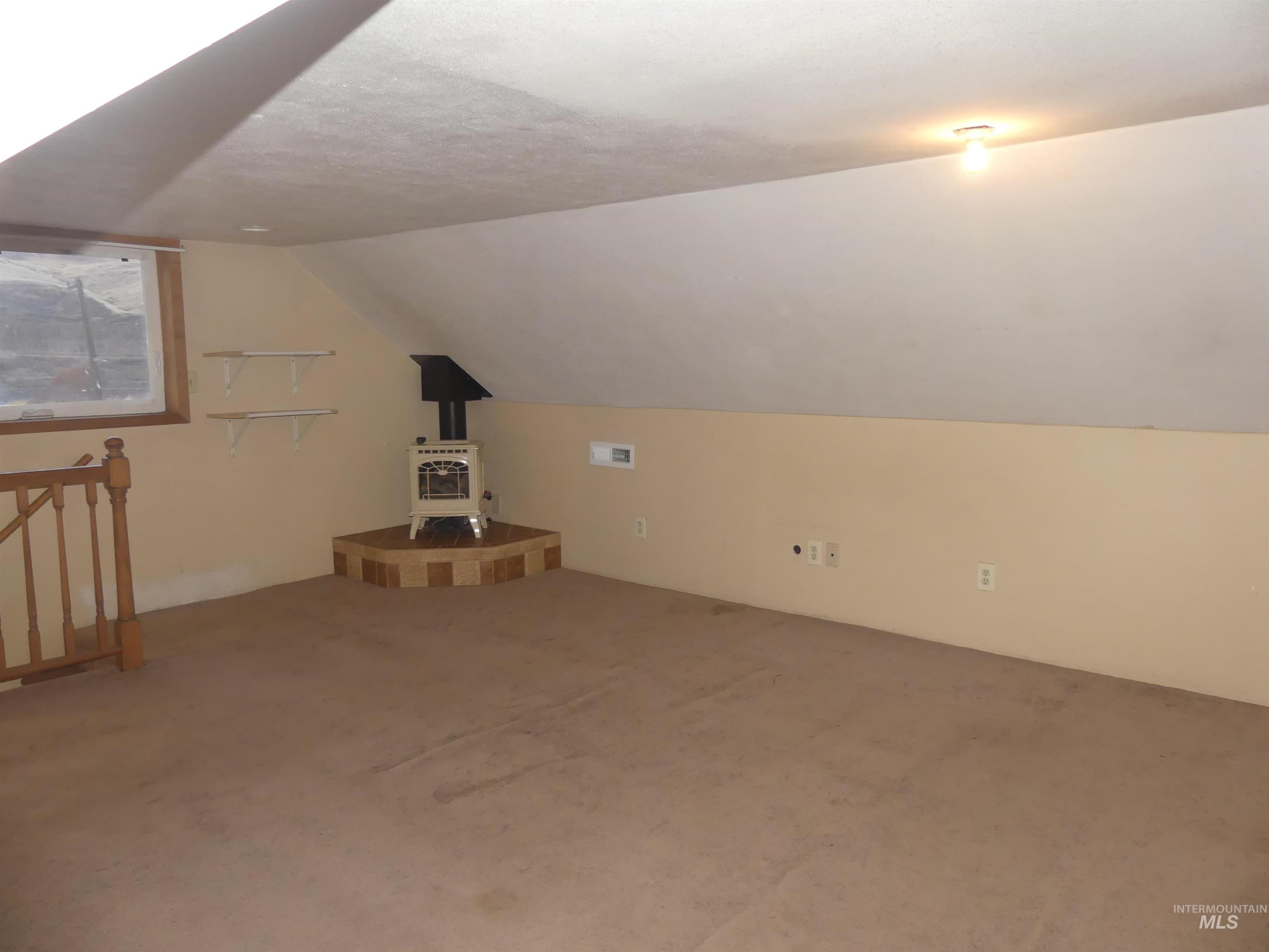 Bonus room featuring a wood stove, carpet floors, vaulted ceiling, and a textured ceiling