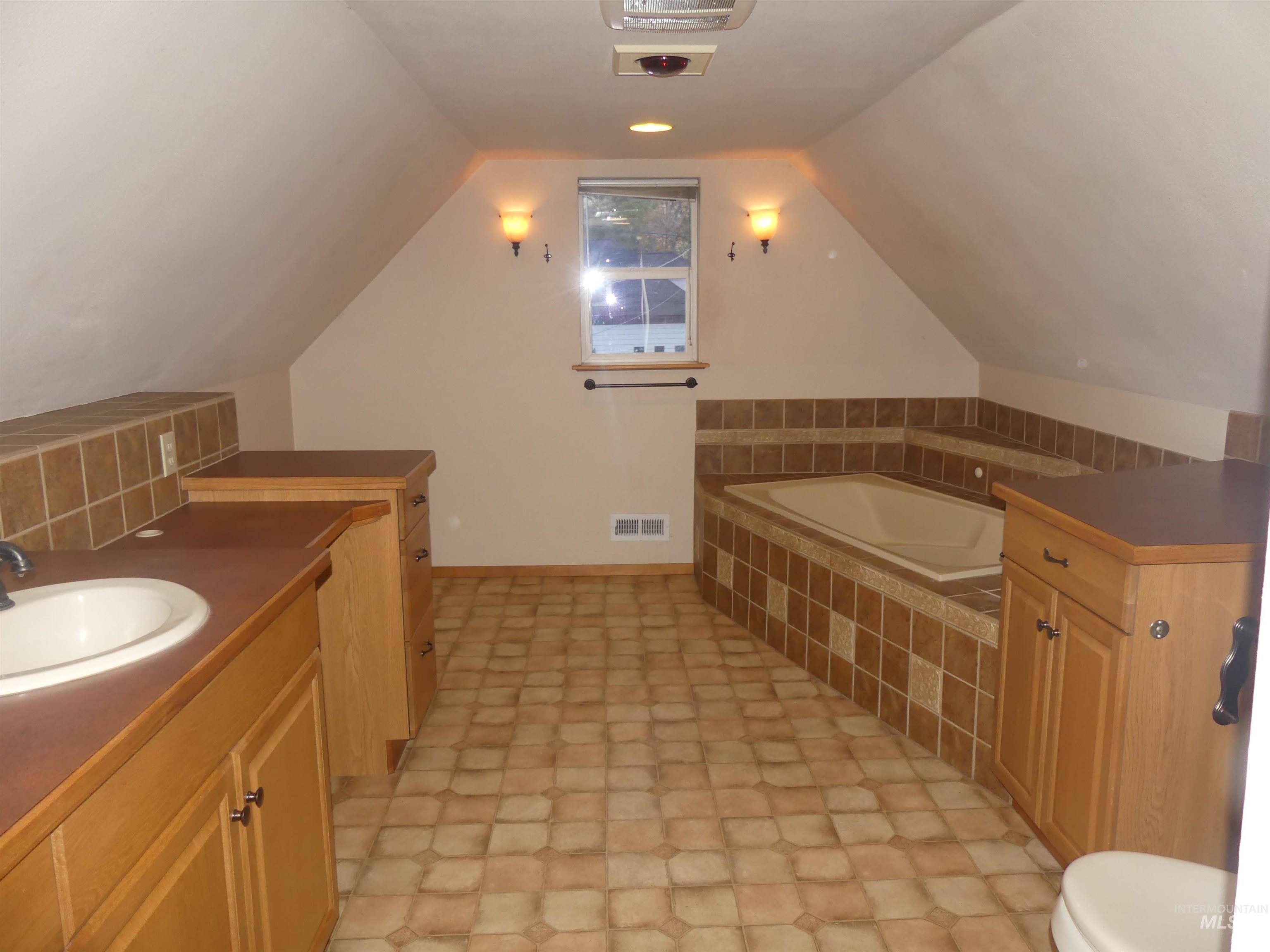 Bathroom with vaulted ceiling, a bath, and vanity