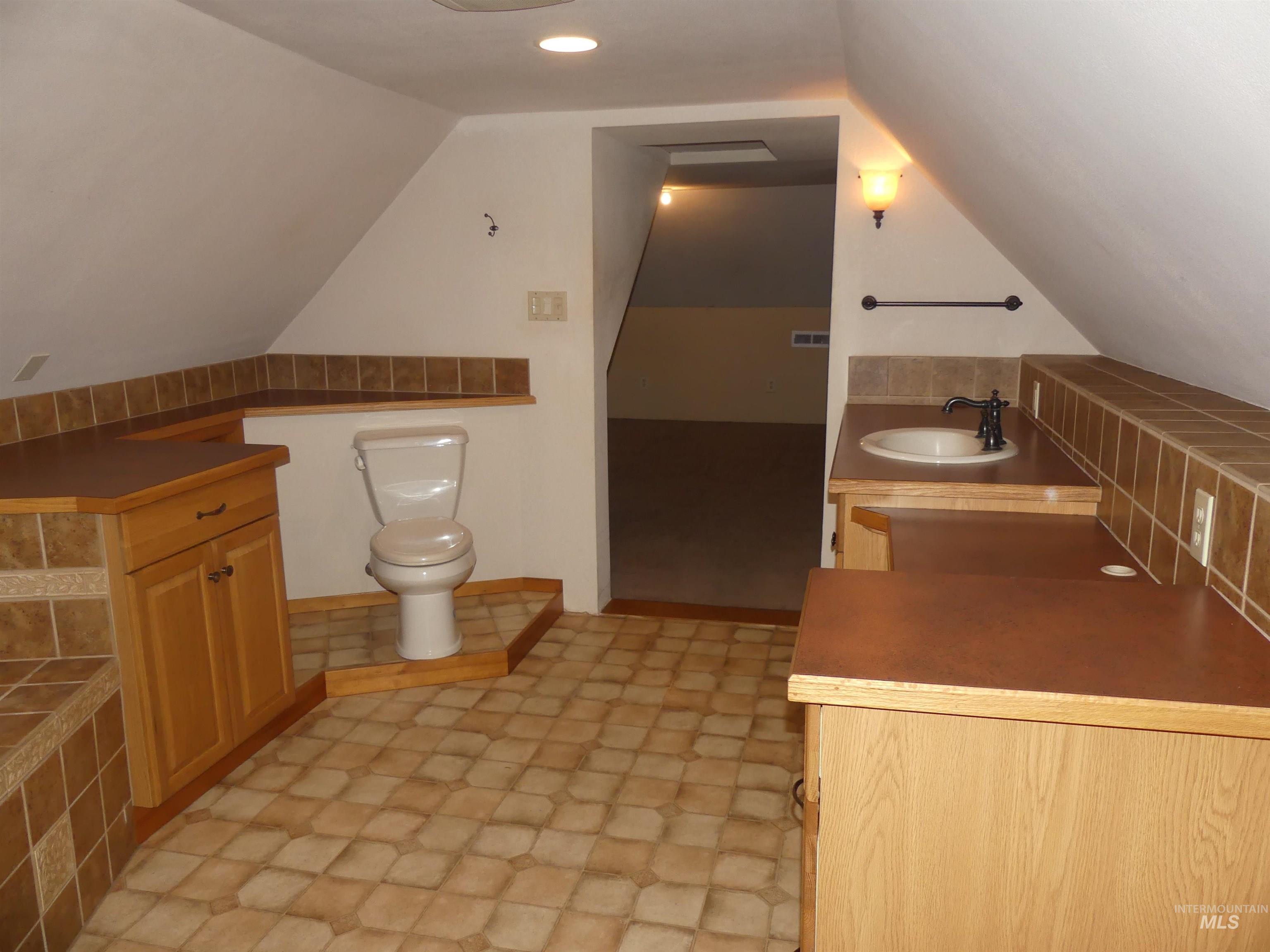 Full bathroom with vaulted ceiling, vanity, and light floors