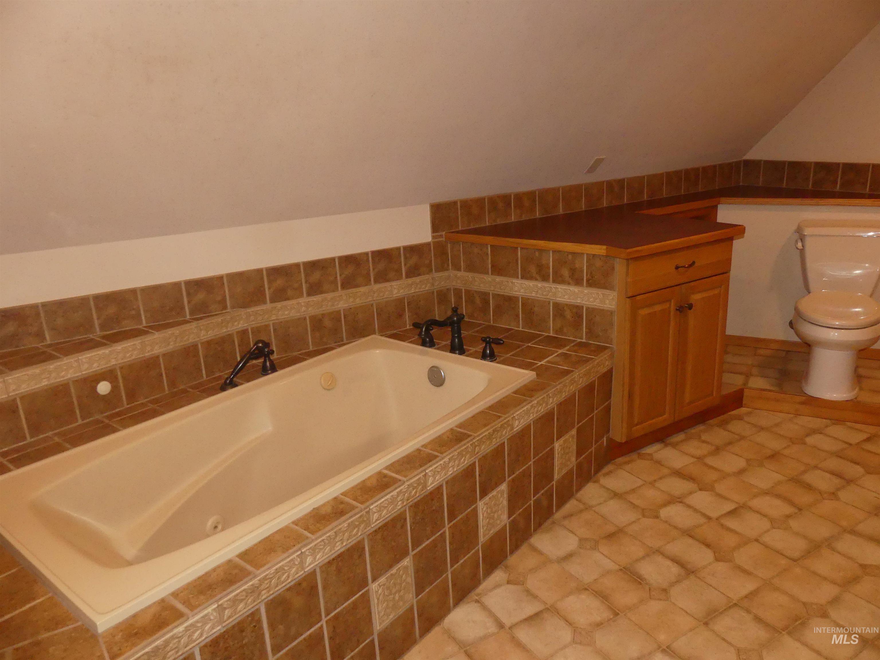 Bathroom with a jetted tub, lofted ceiling, light tile patterned floors, and vanity