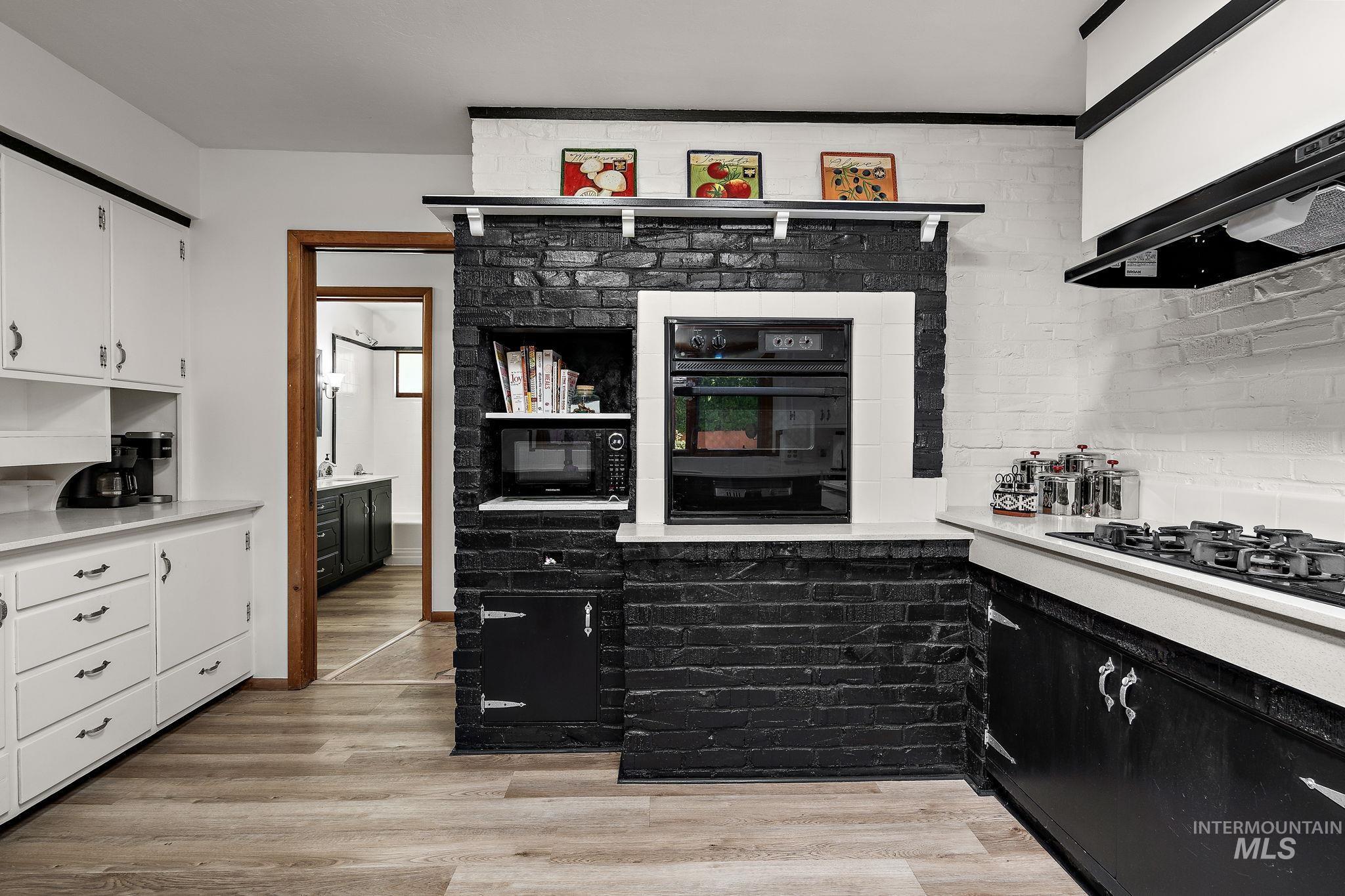 Kitchen featuring light wood-style flooring, black appliances, light countertops, and white cabinets