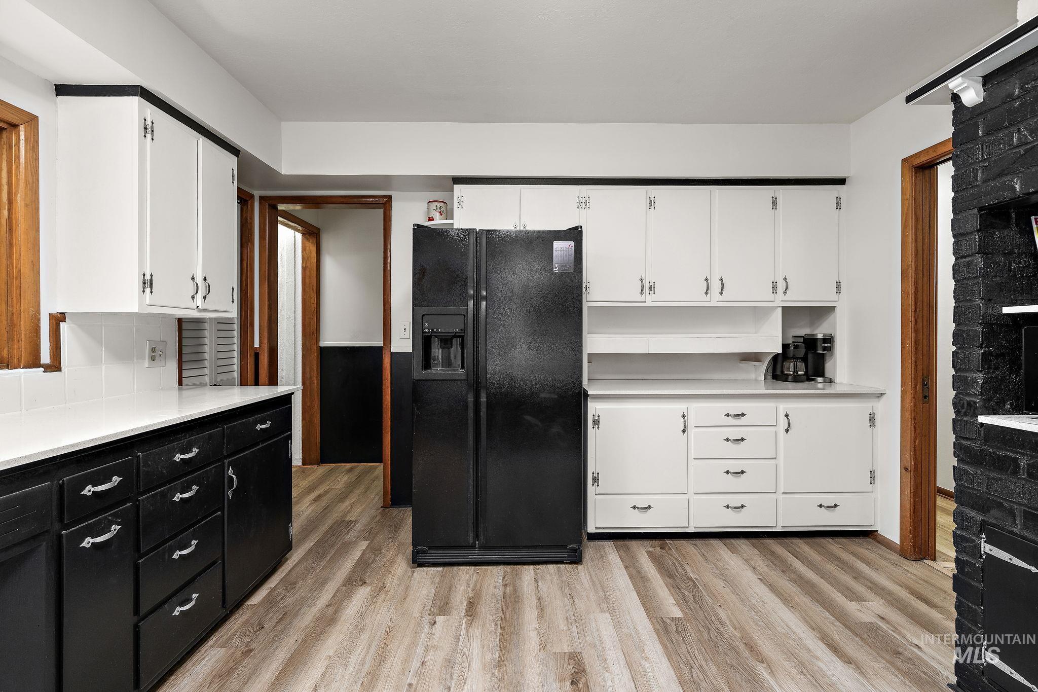 Kitchen featuring black refrigerator with ice dispenser, white cabinetry, light countertops, and light wood-type flooring