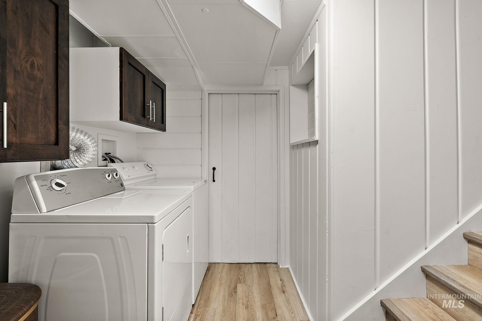 Laundry room featuring cabinet space, separate washer and dryer, light wood finished floors, and wooden walls