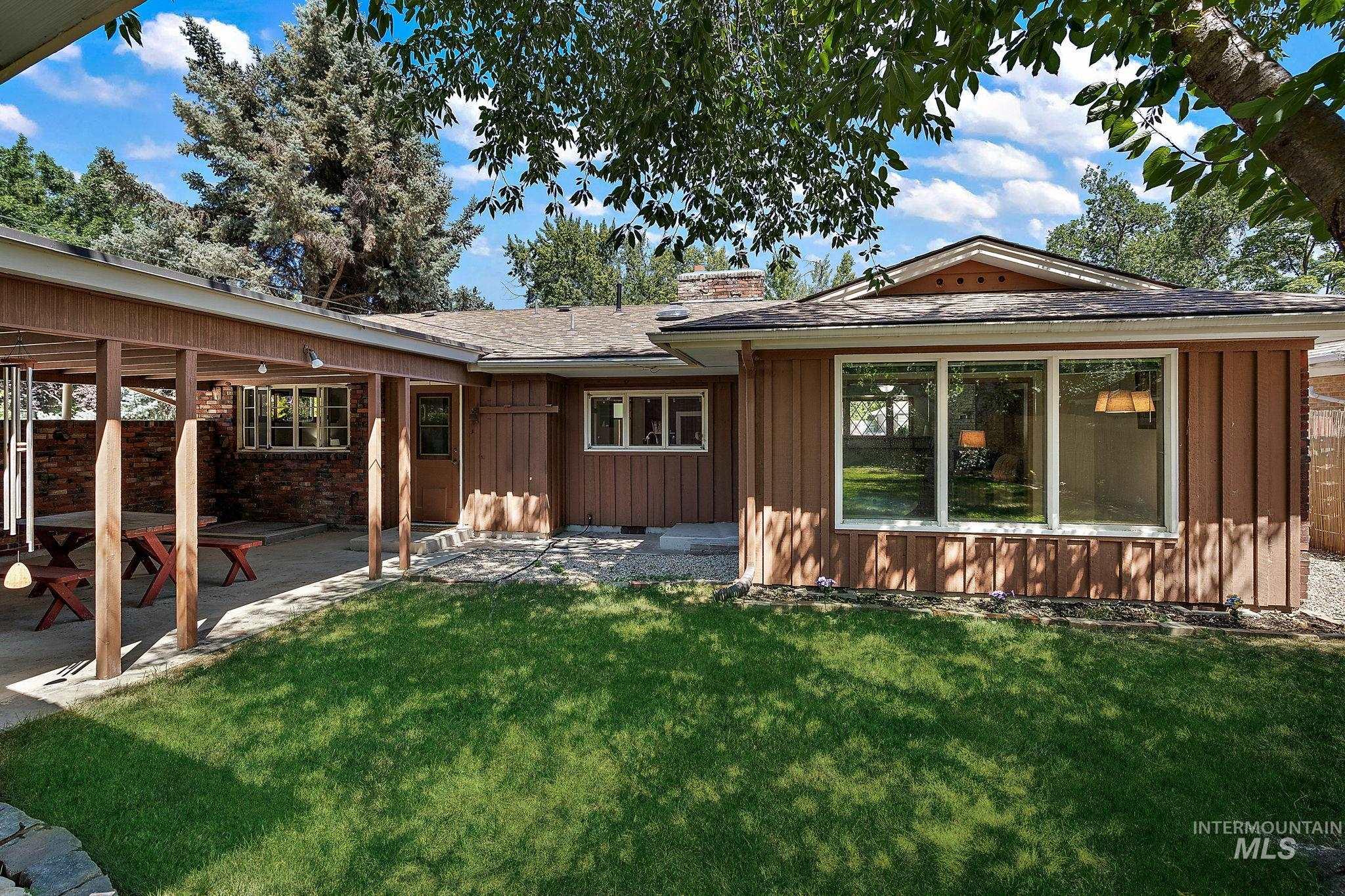 Back of house featuring board and batten siding, a patio area, a lawn, and roof with shingles