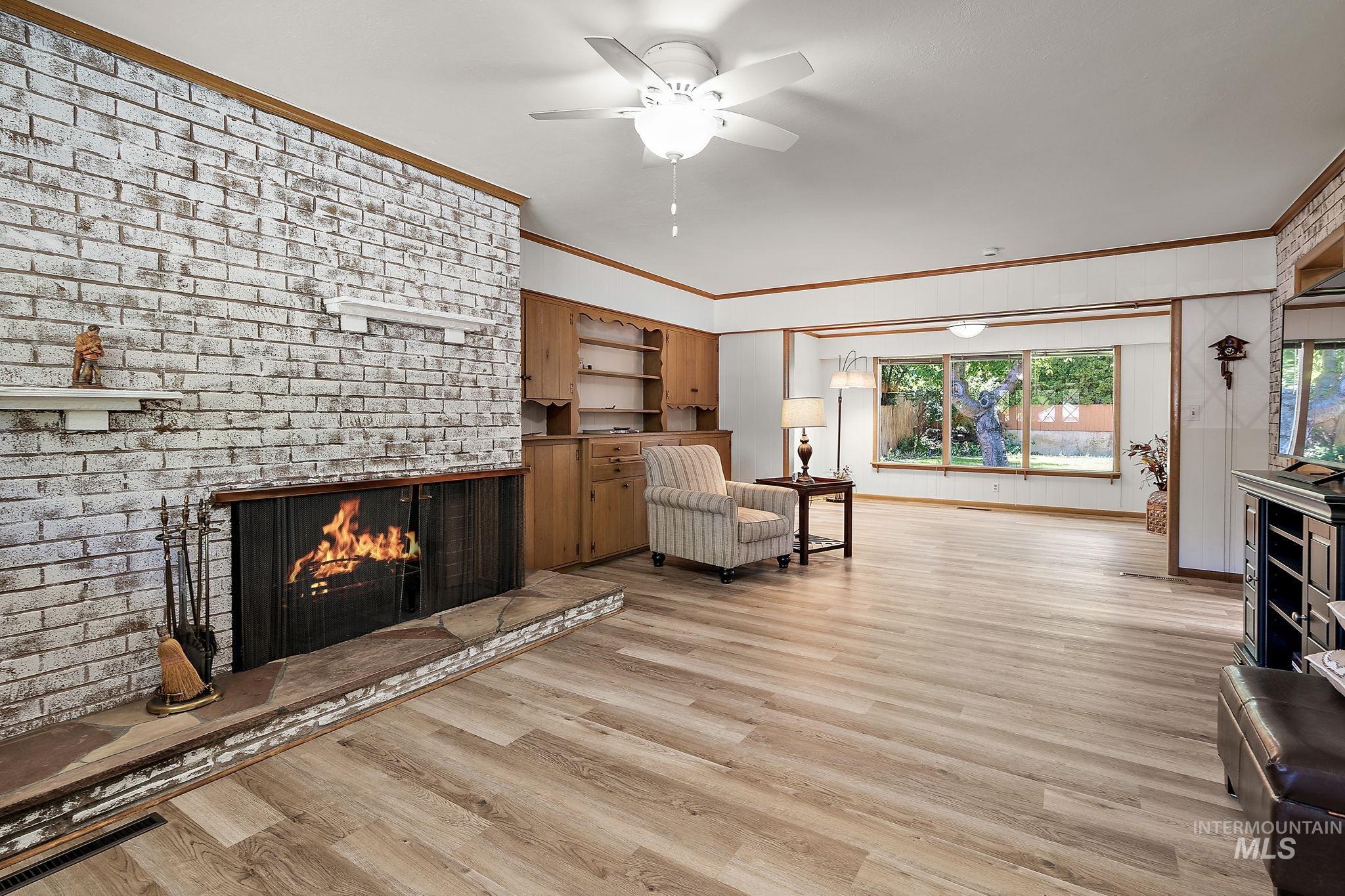 Living area with crown molding, a brick fireplace, light wood-style flooring, ceiling fan, and wooden walls