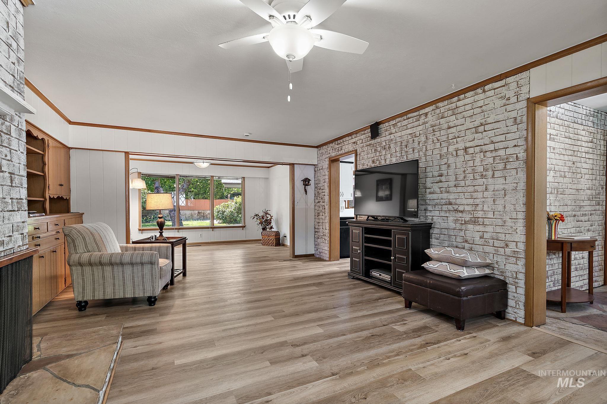 Living room with ornamental molding, brick wall, light wood-style flooring, and a ceiling fan