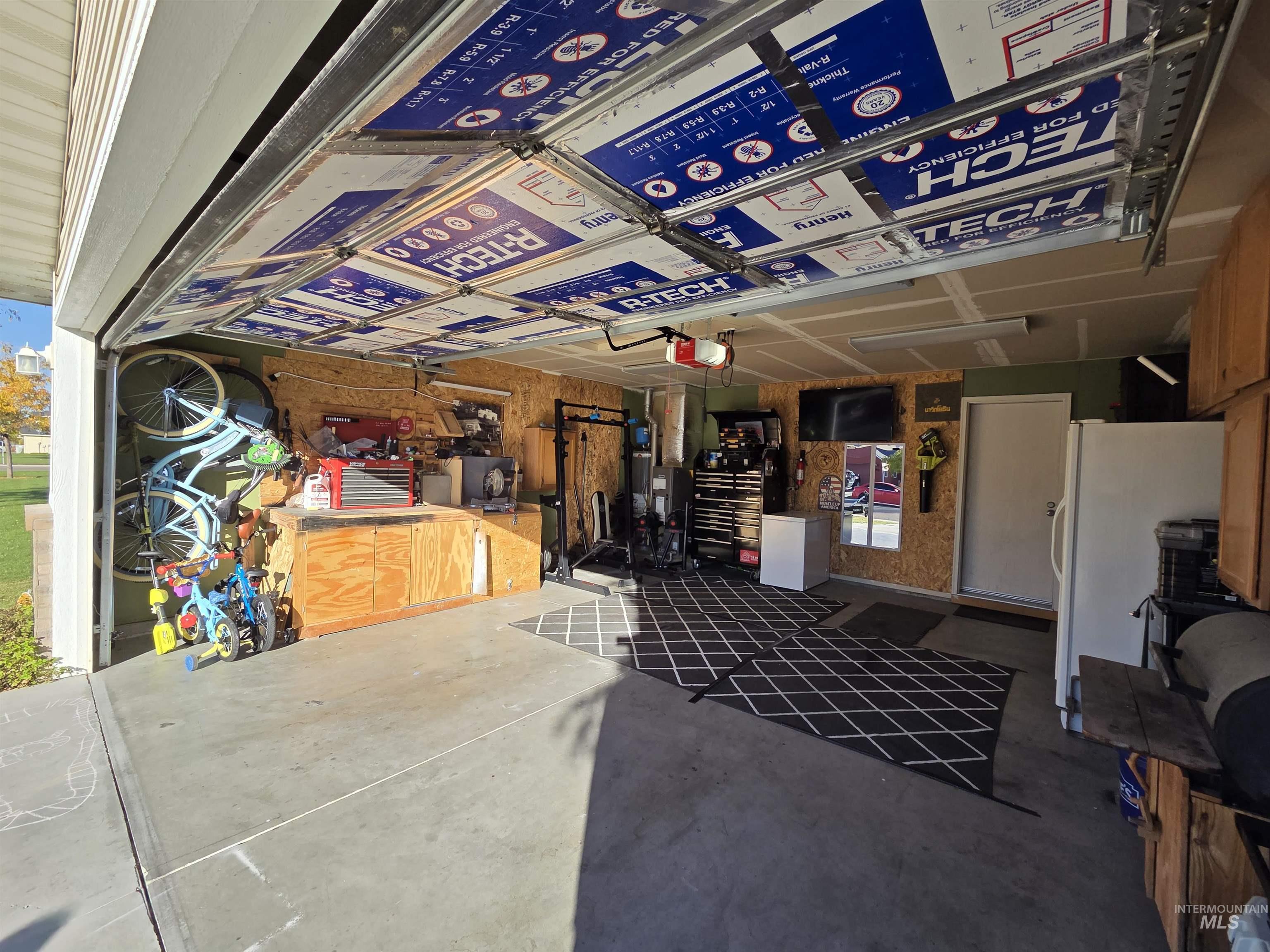 Garage featuring freestanding refrigerator, a garage door opener, and wood walls