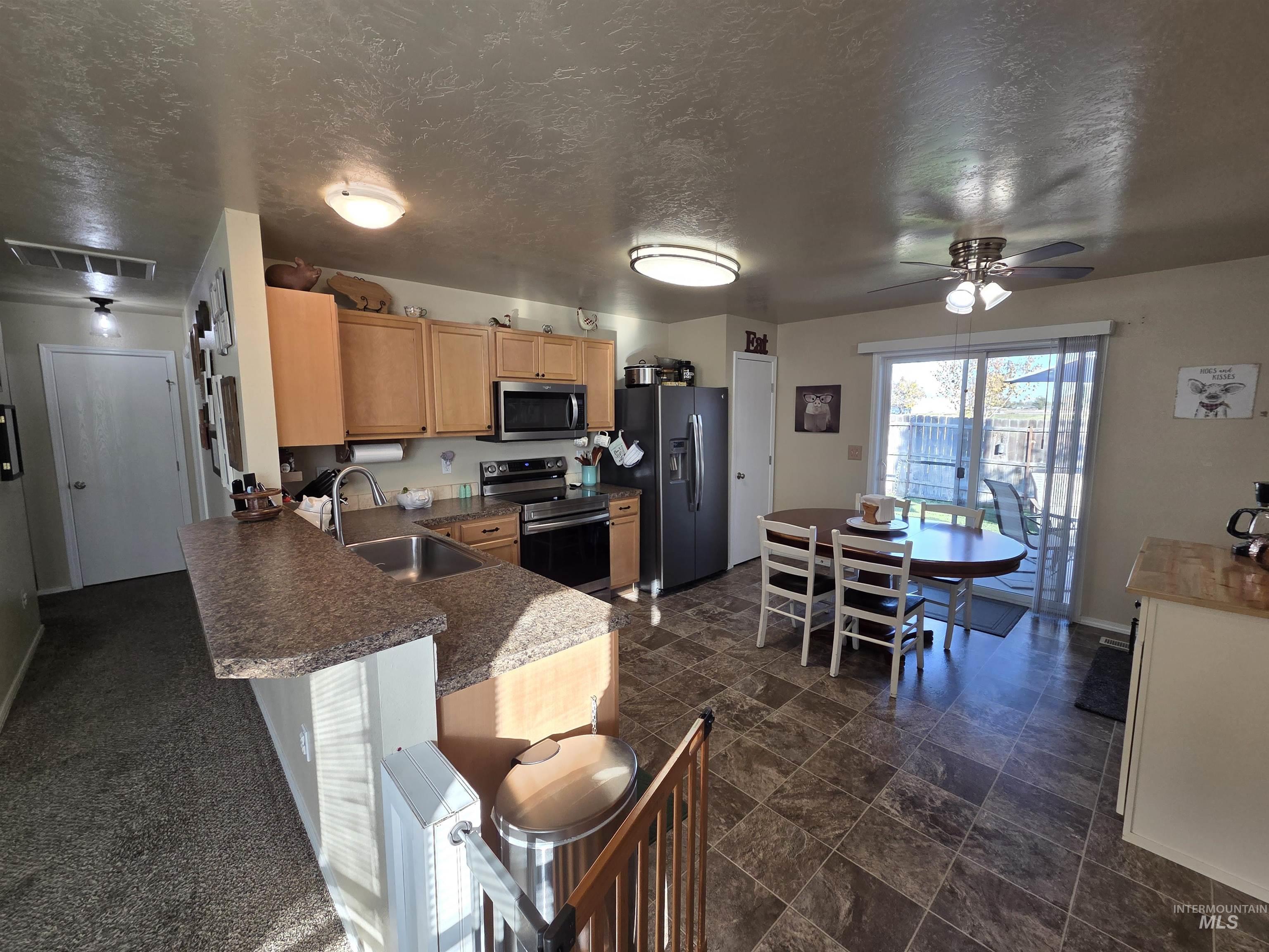 Kitchen with appliances with stainless steel finishes, a textured ceiling, a ceiling fan, a breakfast bar area, and dark countertops