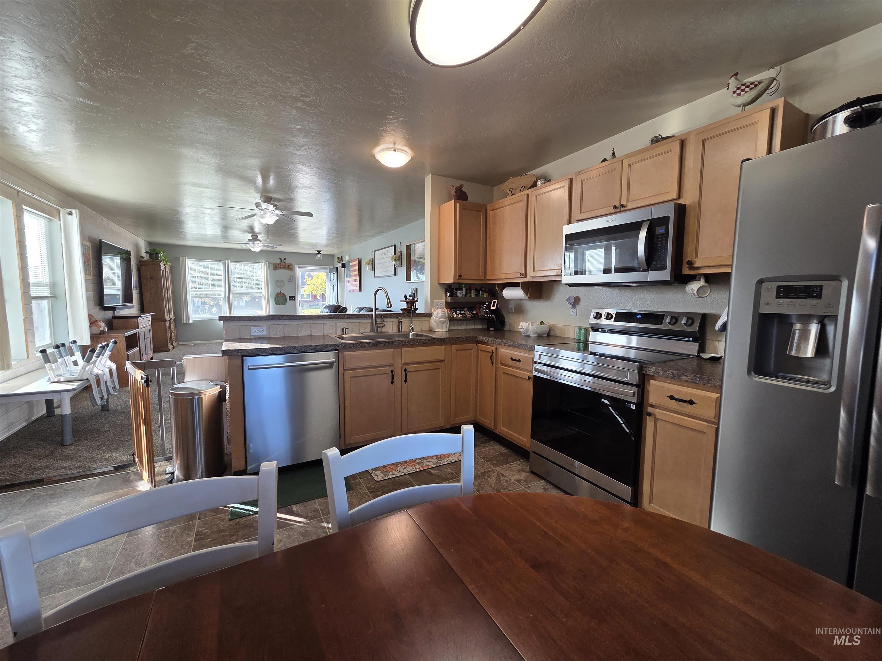 Kitchen with stainless steel appliances, a textured ceiling, open floor plan, a peninsula, and a ceiling fan
