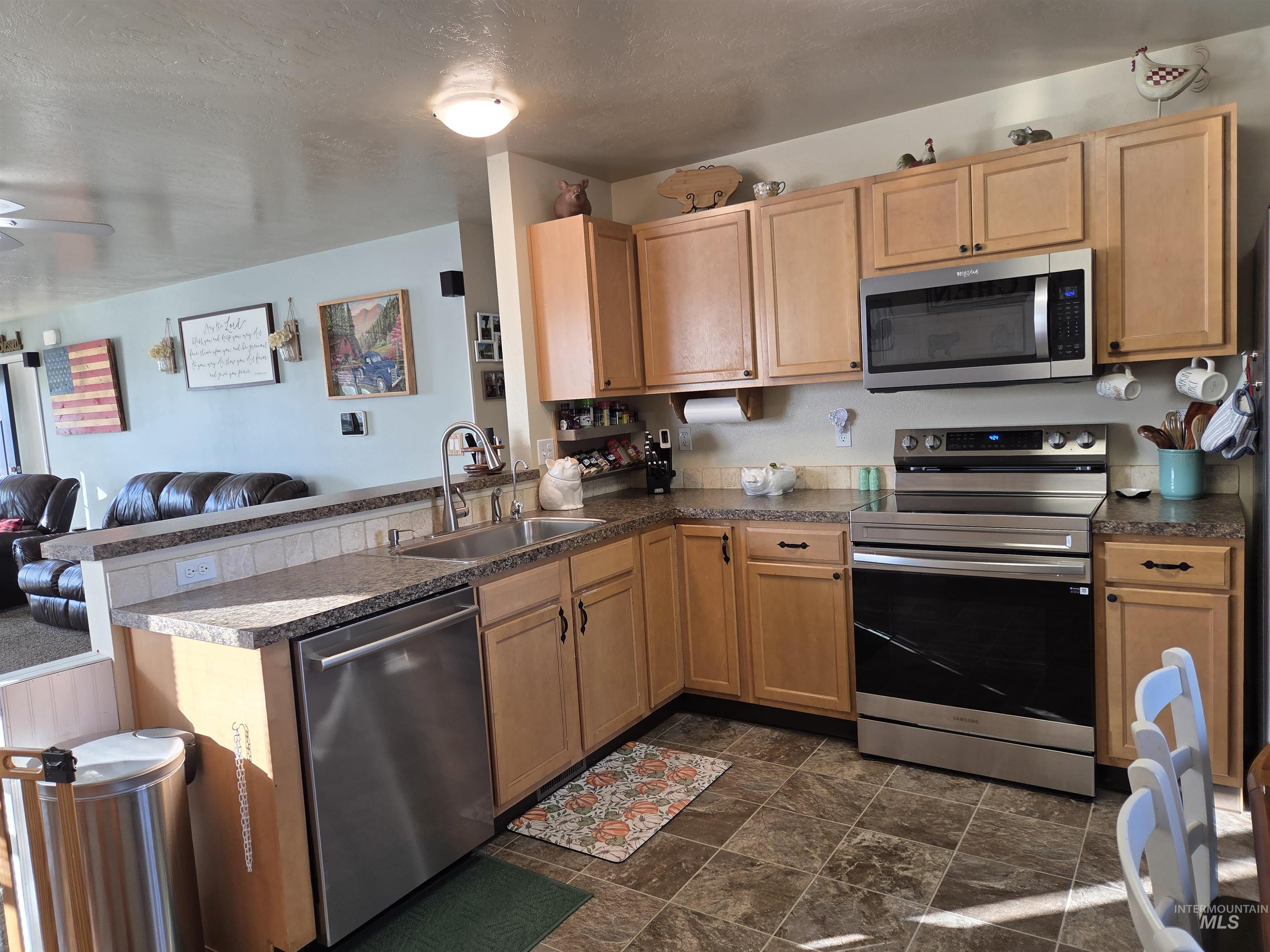 Kitchen with open floor plan, appliances with stainless steel finishes, a peninsula, dark countertops, and a textured ceiling