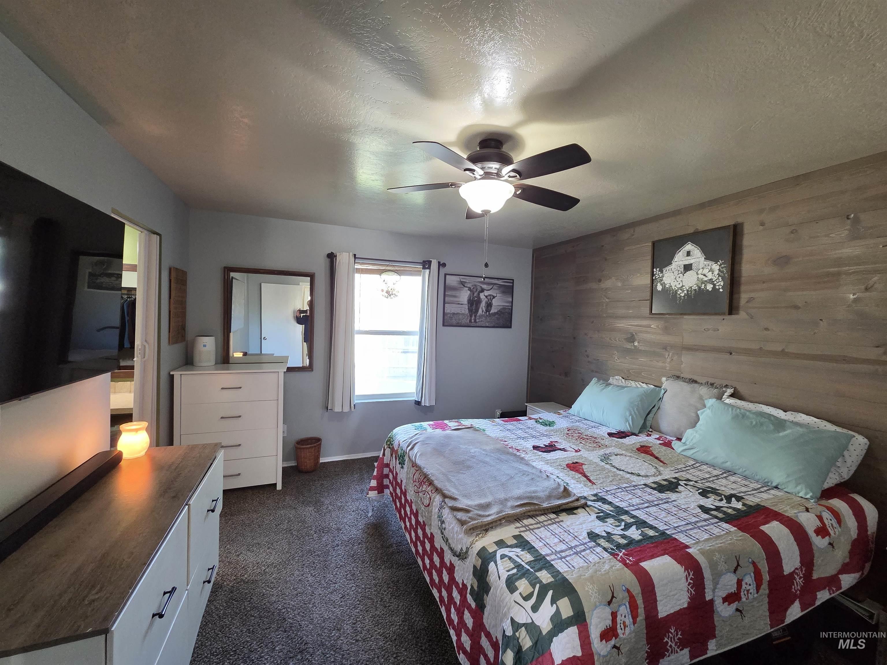Bedroom featuring wood walls, a textured ceiling, a ceiling fan, and dark colored carpet