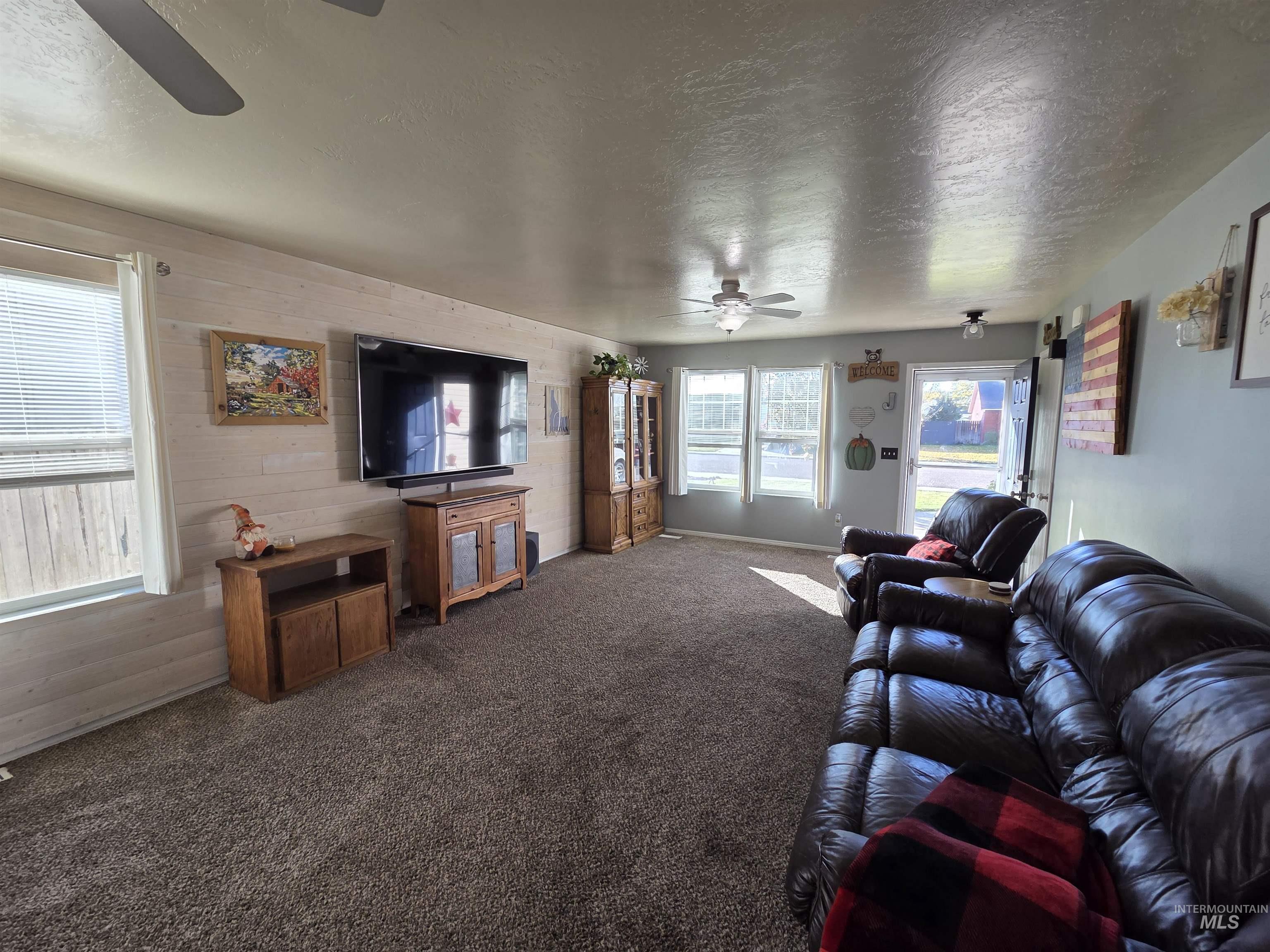 Carpeted living room featuring a textured ceiling, ceiling fan, and wood walls