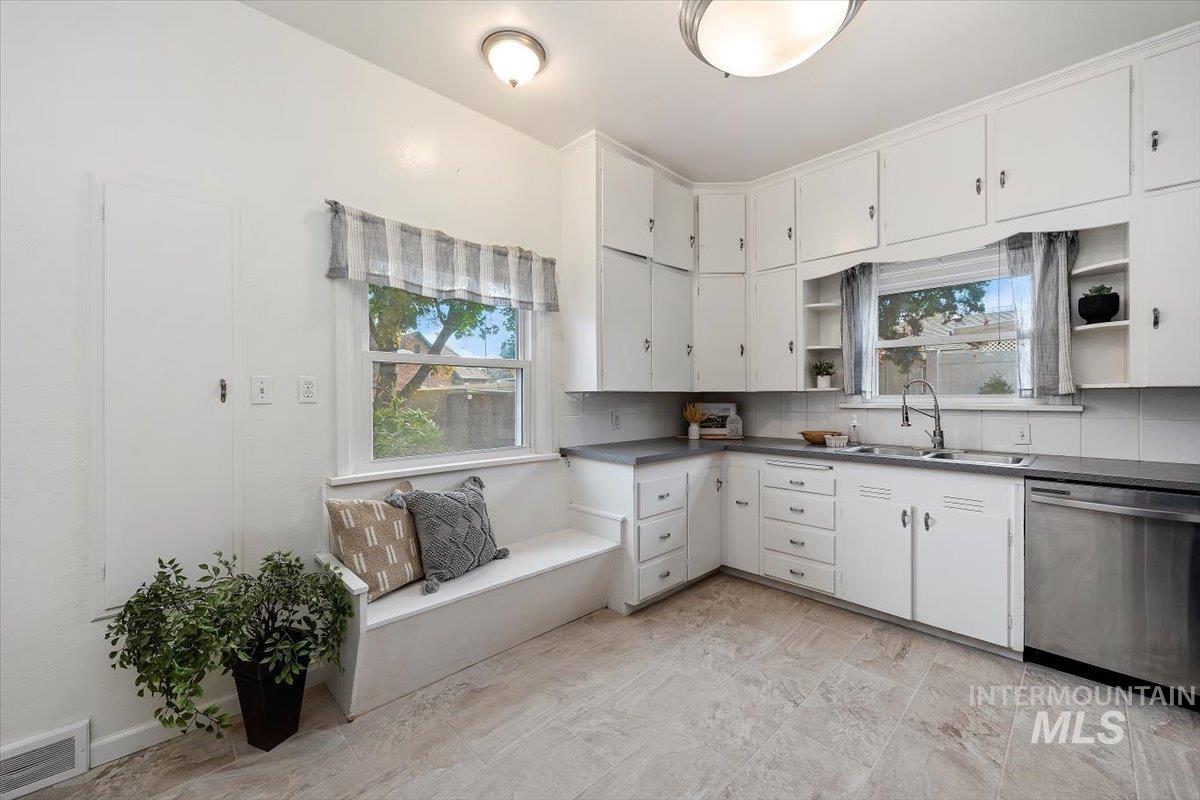 Kitchen featuring open shelves, stainless steel dishwasher, dark countertops, decorative backsplash, and white cabinetry