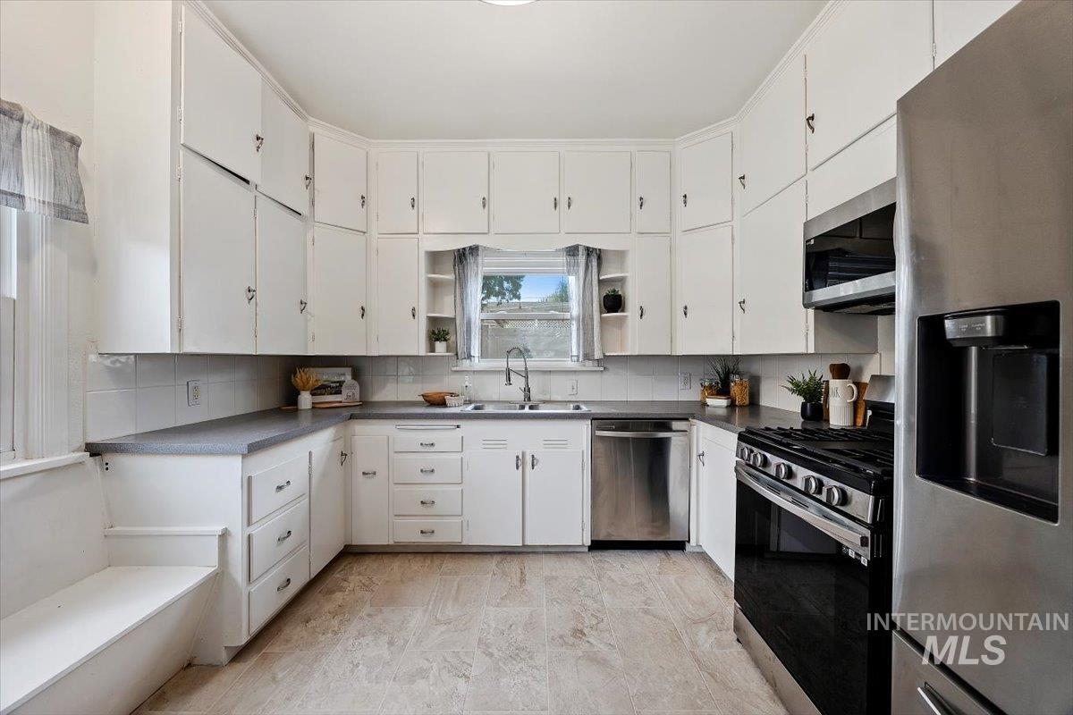 Kitchen featuring appliances with stainless steel finishes, dark countertops, open shelves, and white cabinetry