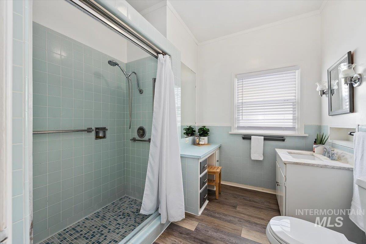 Bathroom featuring dark wood-type flooring, vanity, a shower stall, tile walls, and ornamental molding