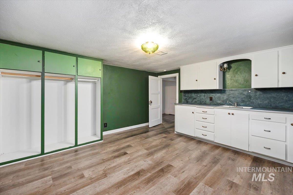 Basement room with white cabinets and sink, featuring backsplash, a textured ceiling, and light wood-type flooring