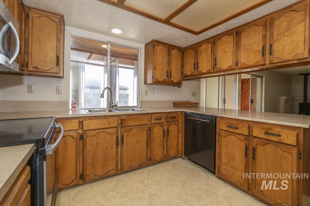 Kitchen with brown cabinetry, stainless steel microwave, a textured ceiling, light countertops, and dishwasher