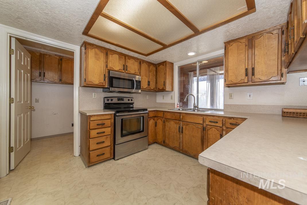 Kitchen featuring brown cabinets, a textured ceiling, stainless steel appliances, light countertops, and light floors