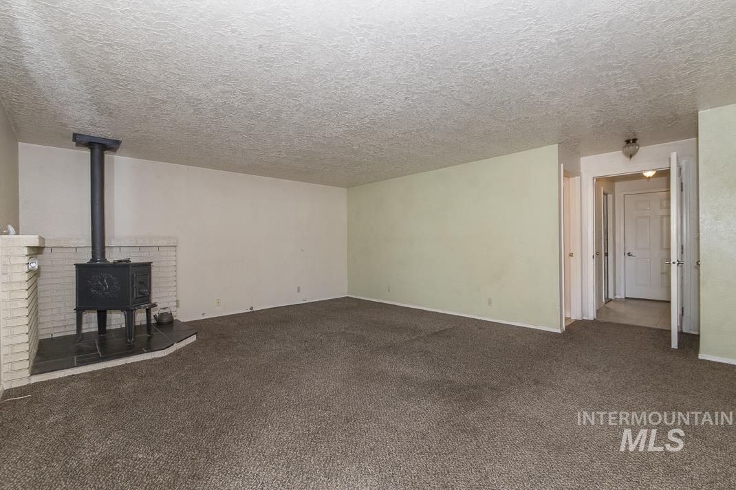 Unfurnished living room with a wood stove, dark colored carpet, and a textured ceiling