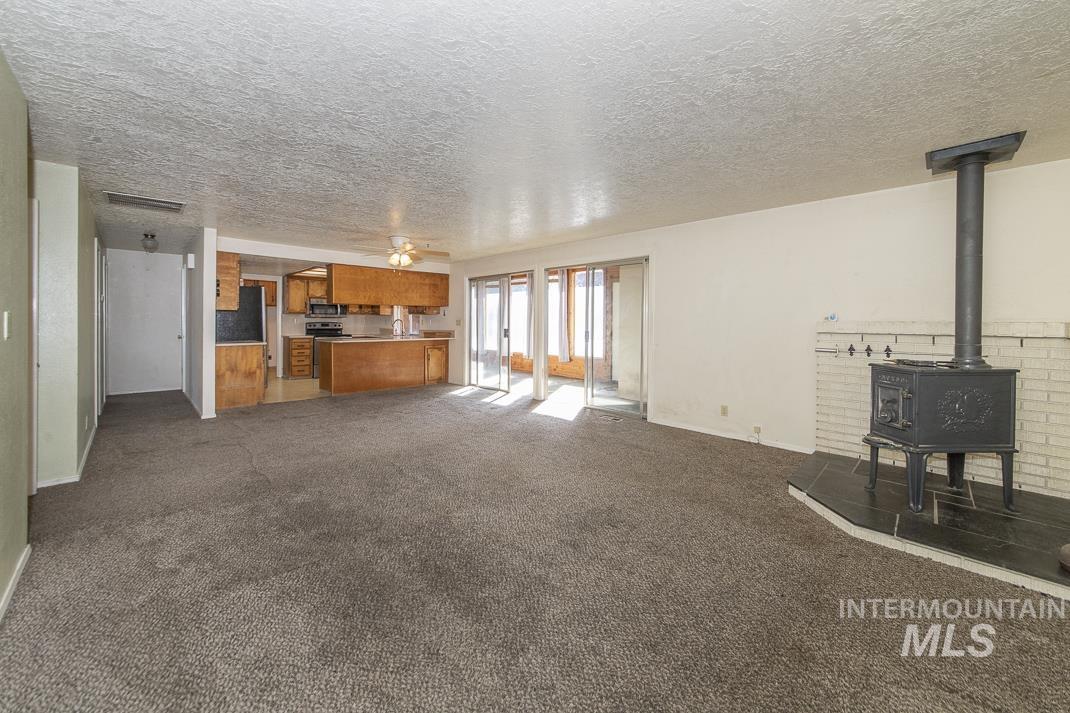 Unfurnished living room with a wood stove, dark carpet, a textured ceiling, and ceiling fan