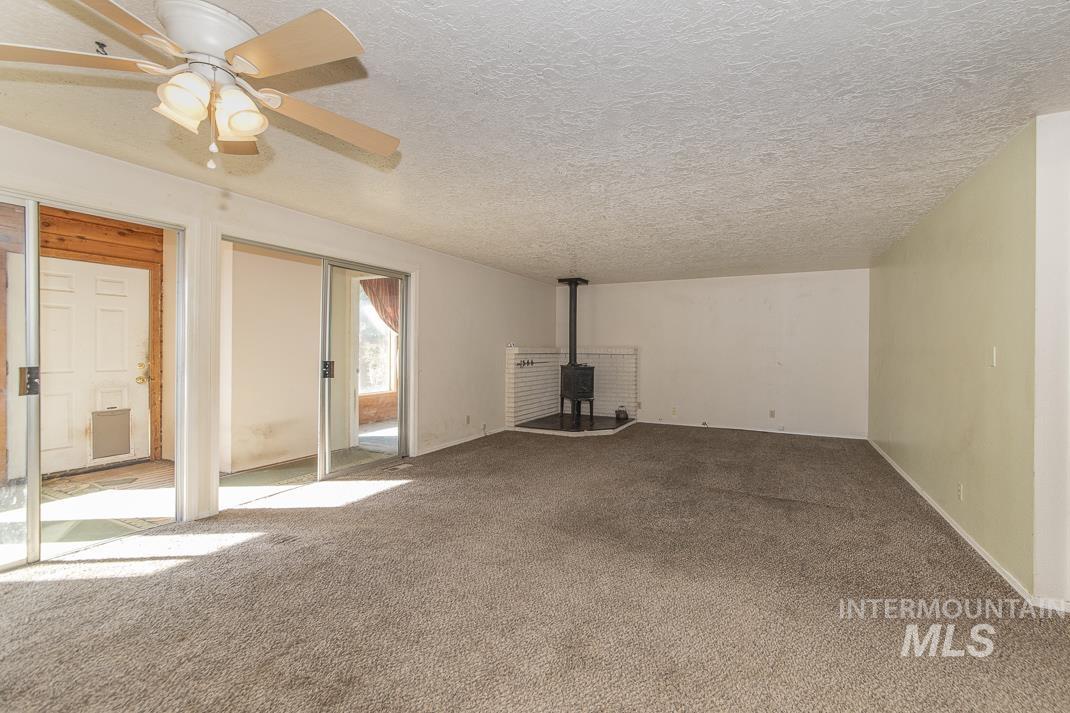 Unfurnished living room with a wood stove, carpet, a textured ceiling, and ceiling fan