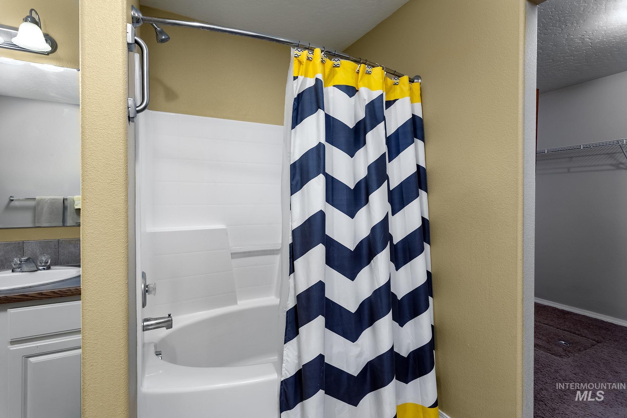 Full bathroom featuring a walk in closet, shower / tub combo with curtain, vanity, and a textured ceiling
