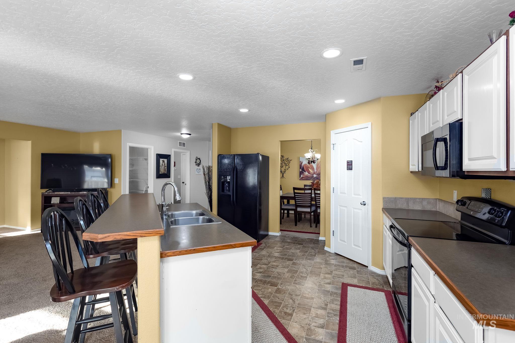 Kitchen featuring black appliances, dark countertops, a breakfast bar area, a kitchen island with sink, and stone finish flooring