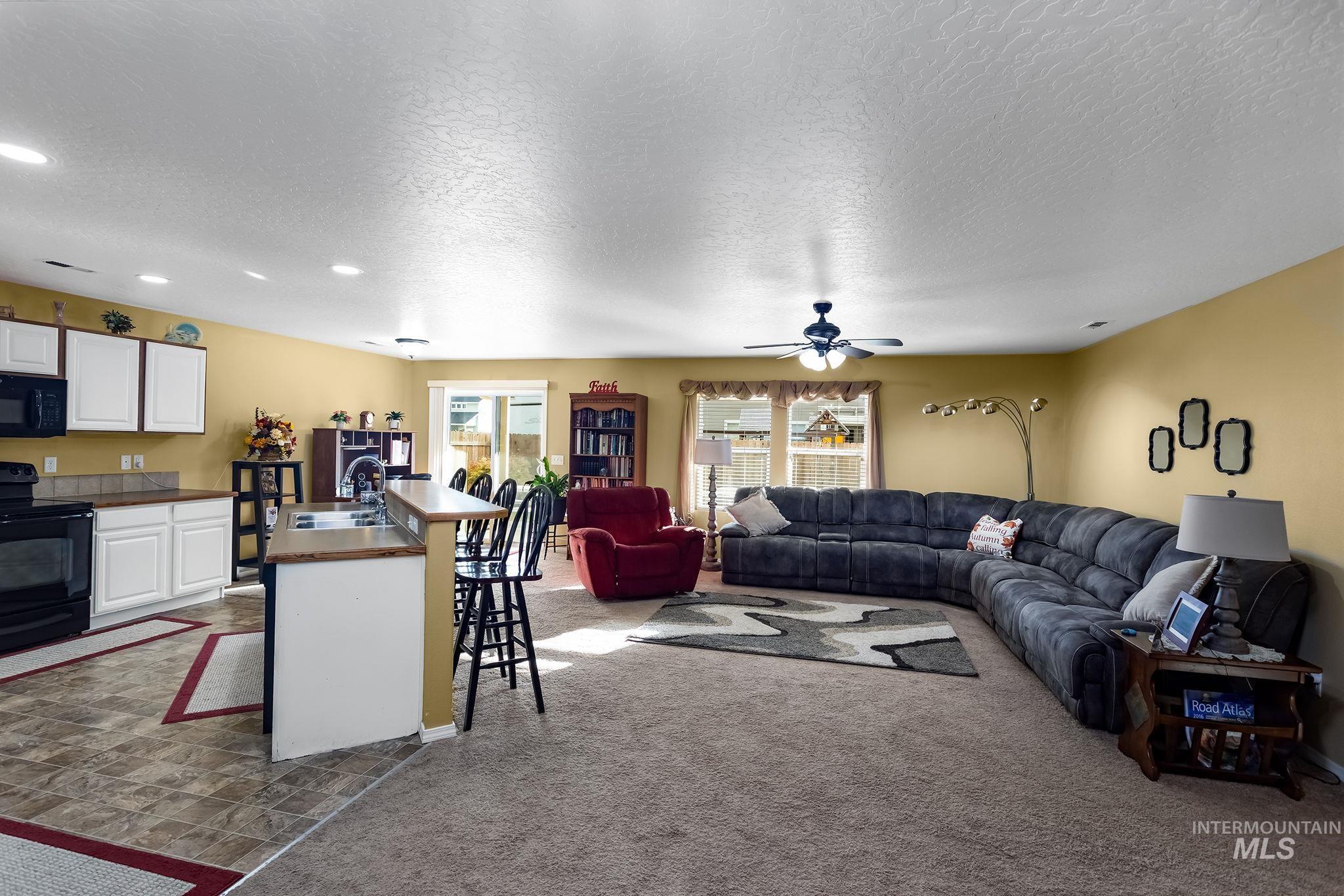 Living area with dark colored carpet, a textured ceiling, and a ceiling fan