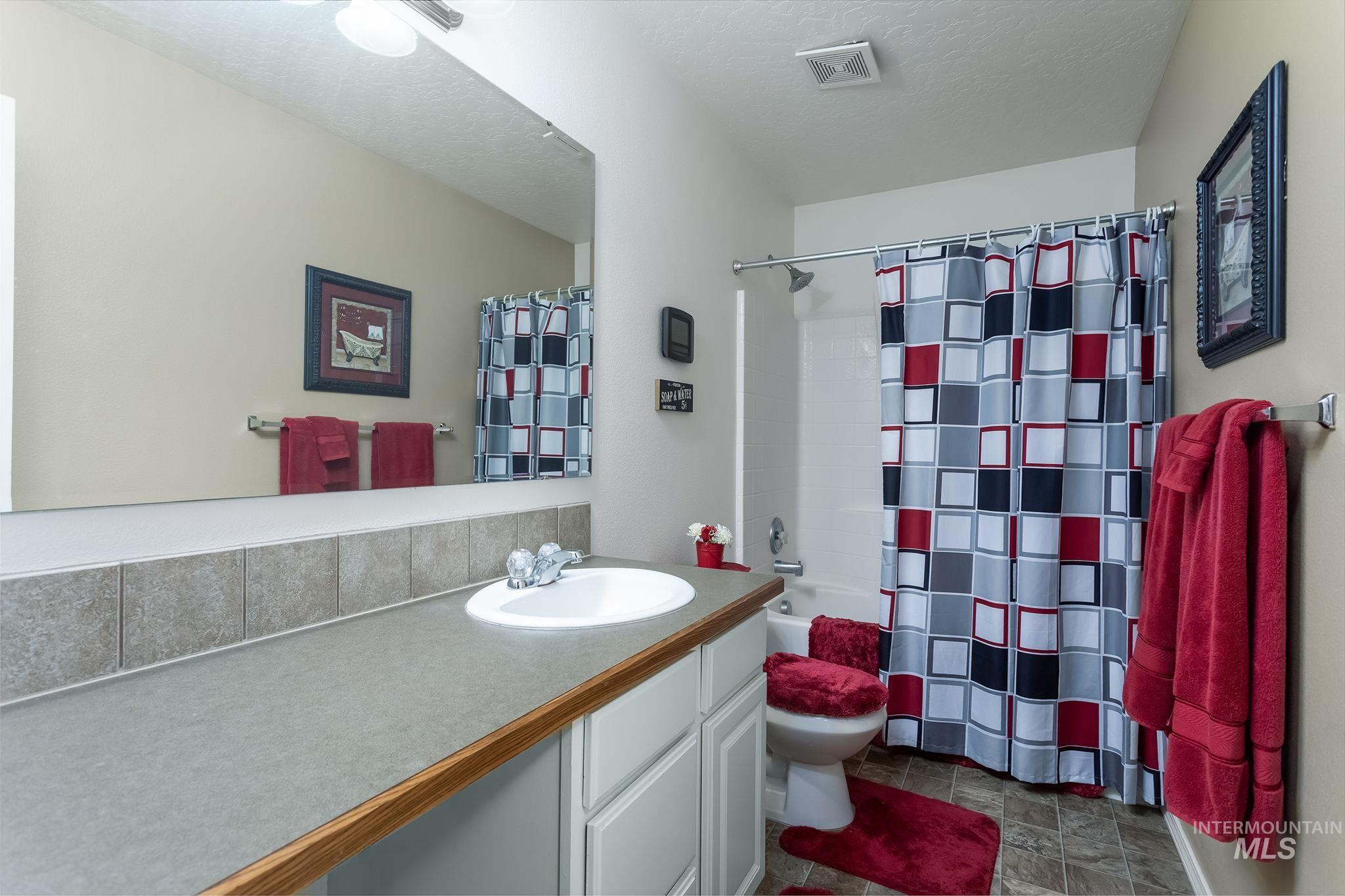 Full bath with a textured ceiling, vanity, and shower / bath combination with curtain