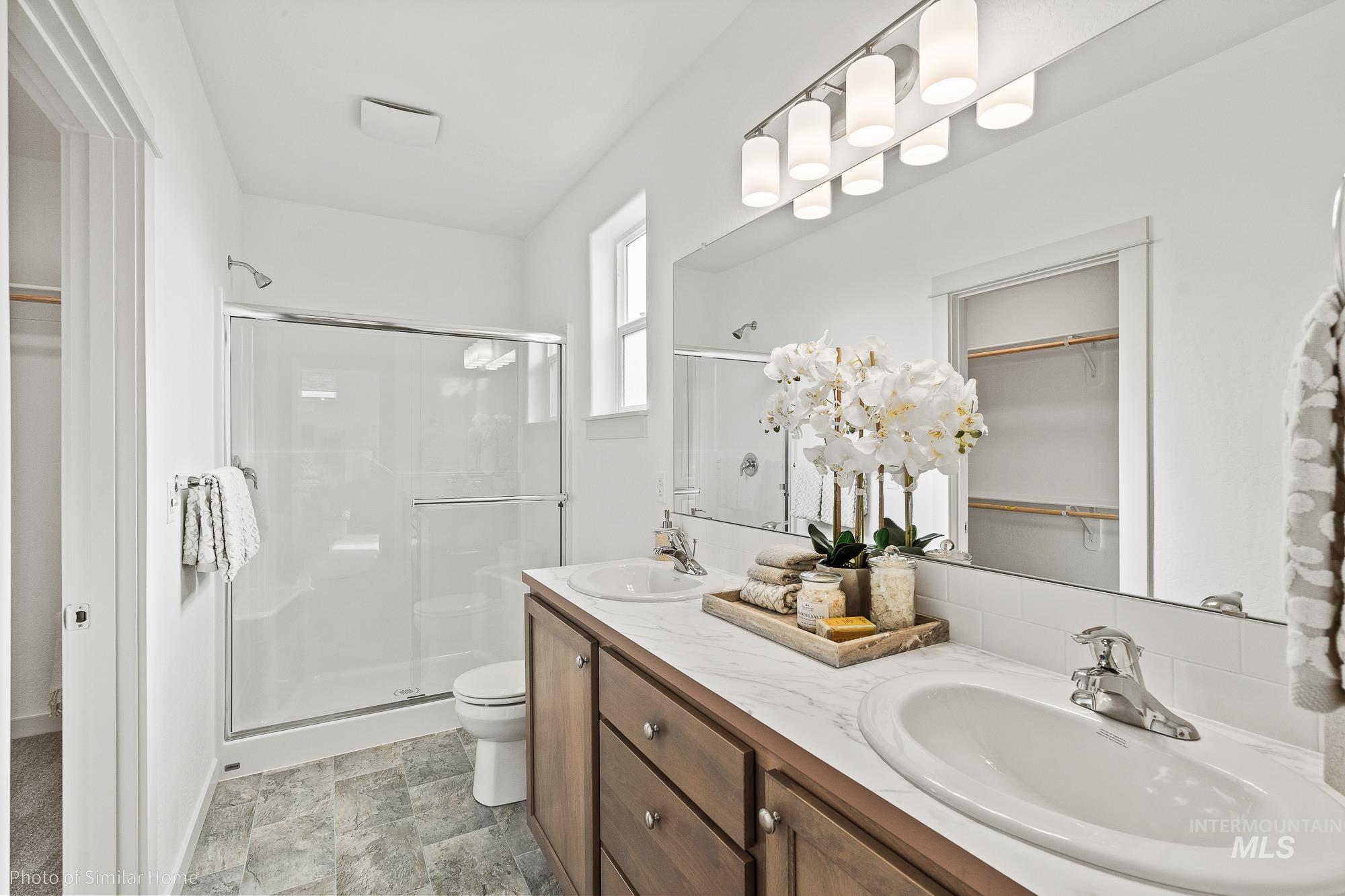 Full bath featuring a shower stall, a spacious closet, double vanity, and stone finish floors