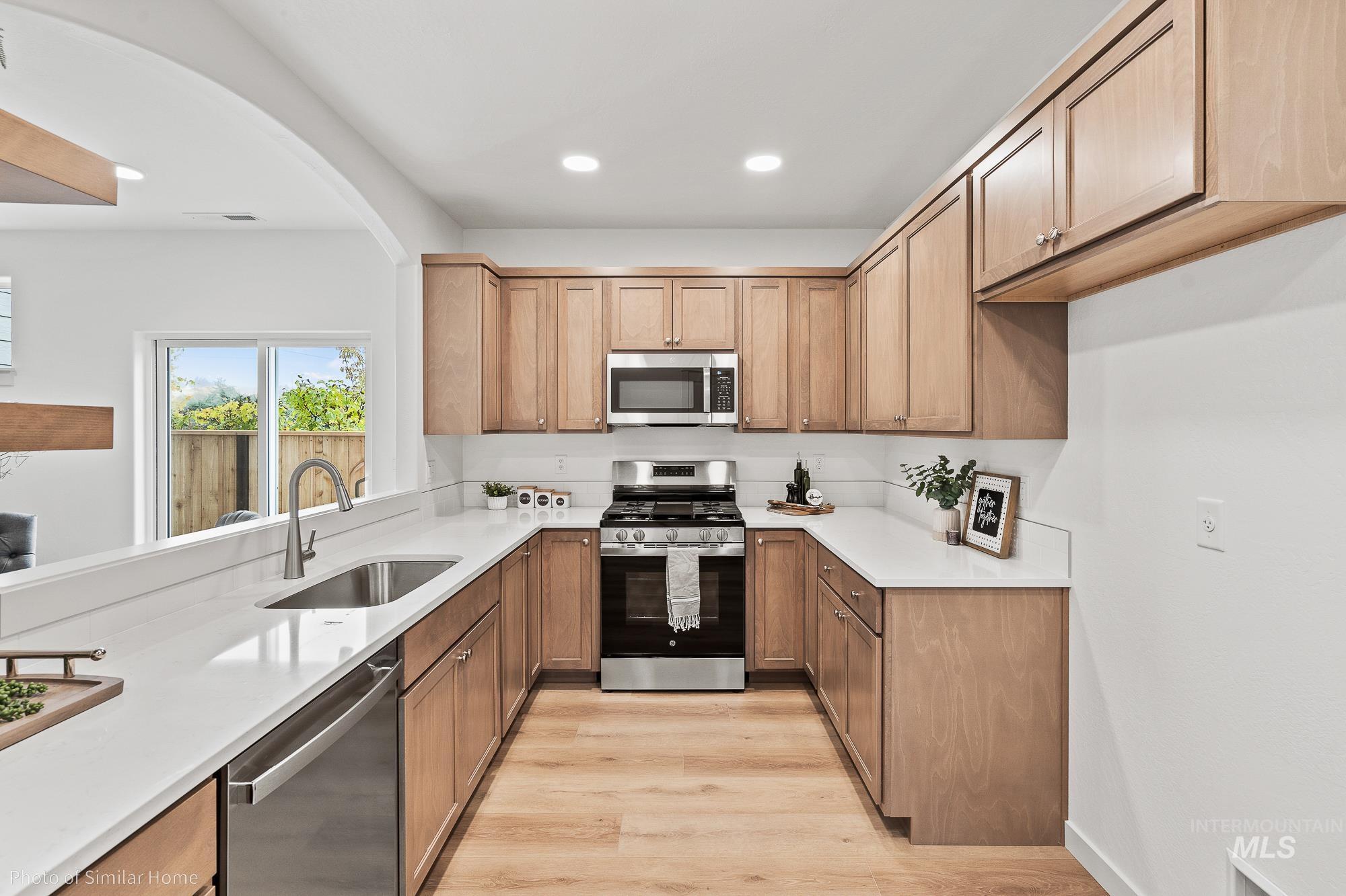 Kitchen with stainless steel appliances, arched walkways, light wood finished floors, light countertops, and recessed lighting