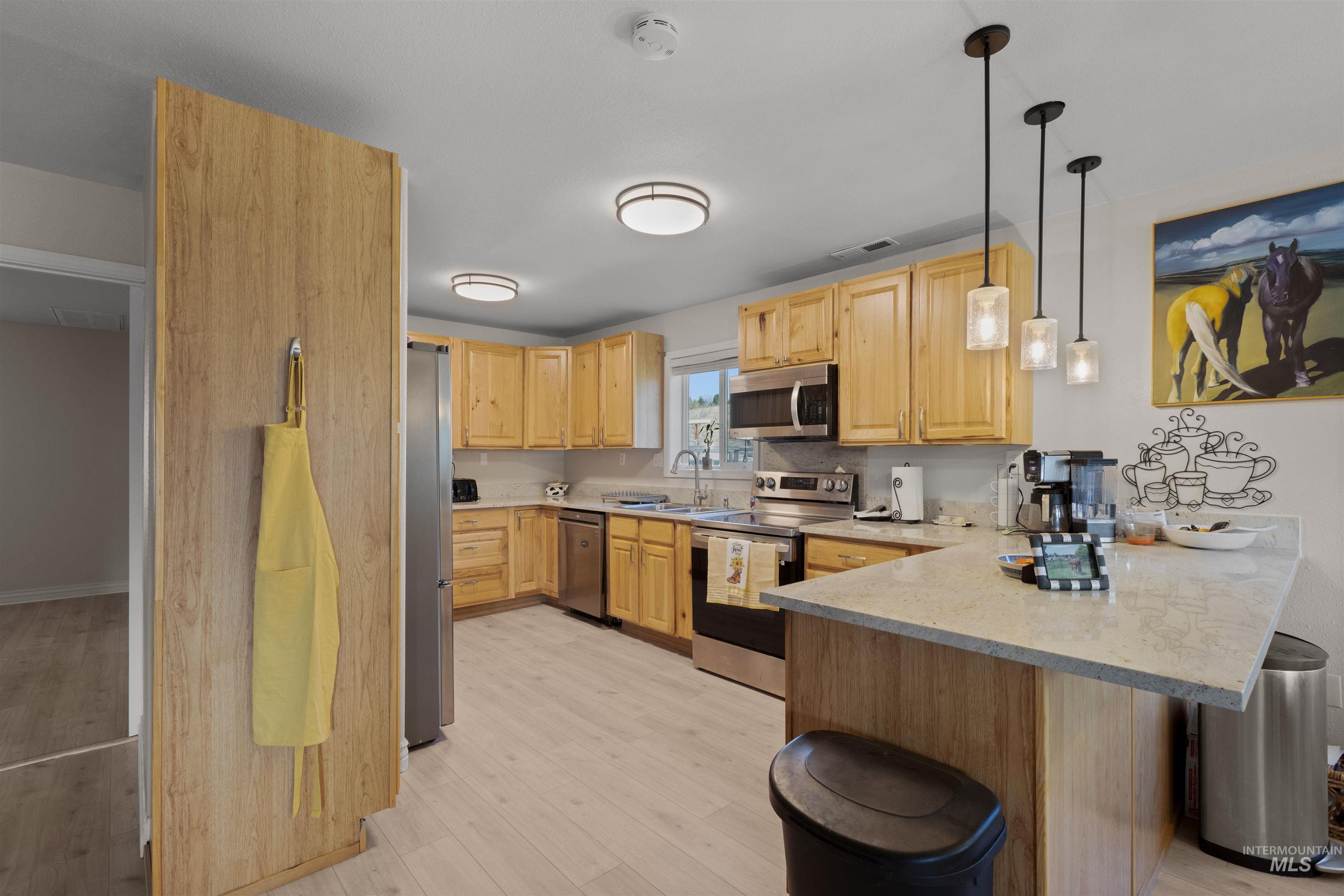 Kitchen featuring appliances with stainless steel finishes, light wood-style flooring, decorative light fixtures, a peninsula, and decorative backsplash